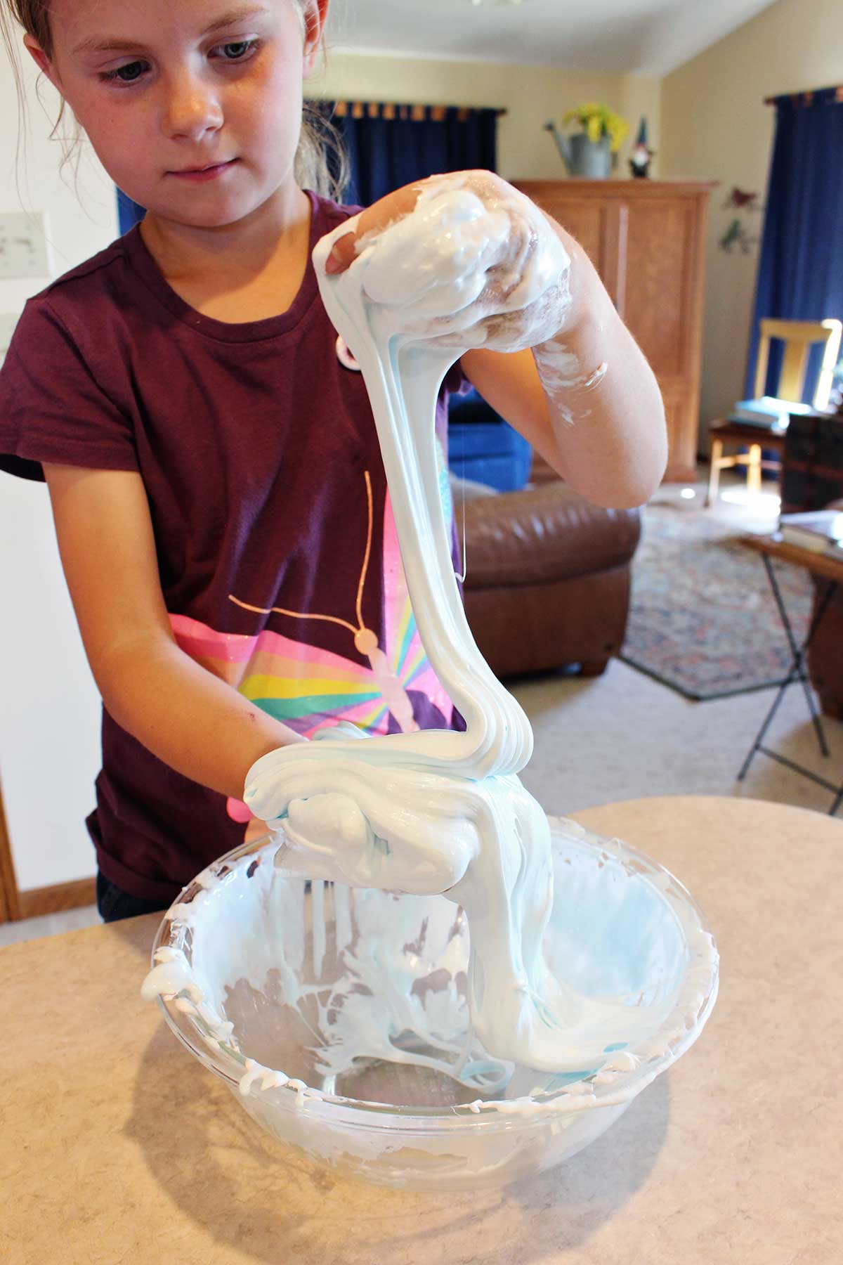 Menina jovem com camisa de borboleta marrom brincando com uma porção de slime fofa em uma tigela de vidro.