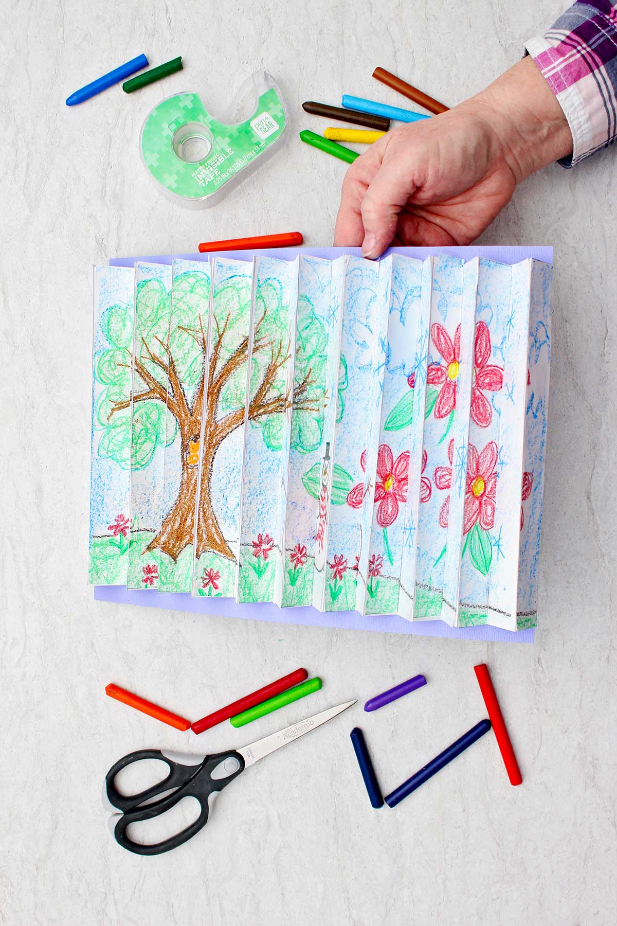 Pessoa segurando a imagem do agamógrafo concluído em um ângulo para ver a imagem de uma árvore na estação primavera com suprimentos ao redor.