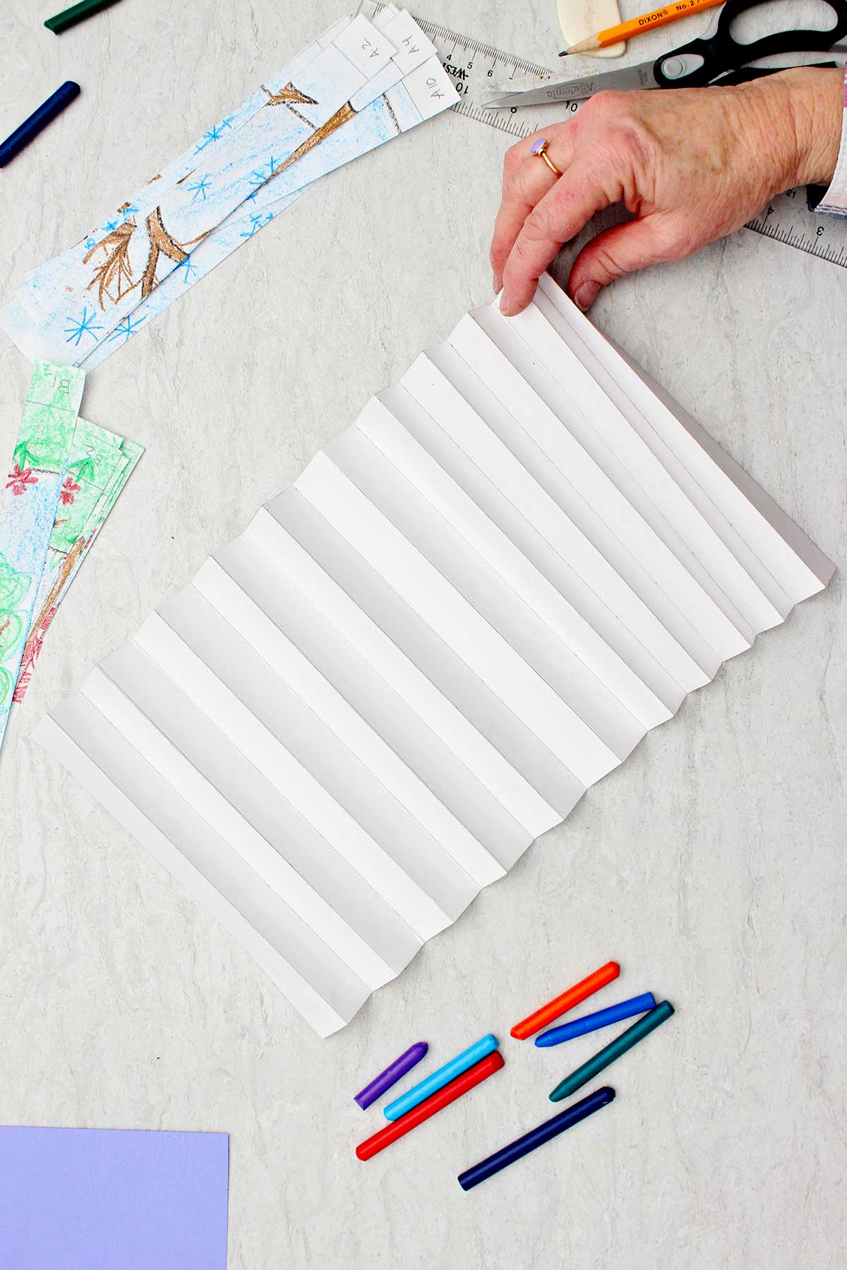 Pessoa dobrando uma longa peça de papel branco como um acordeão com outros suprimentos por perto.