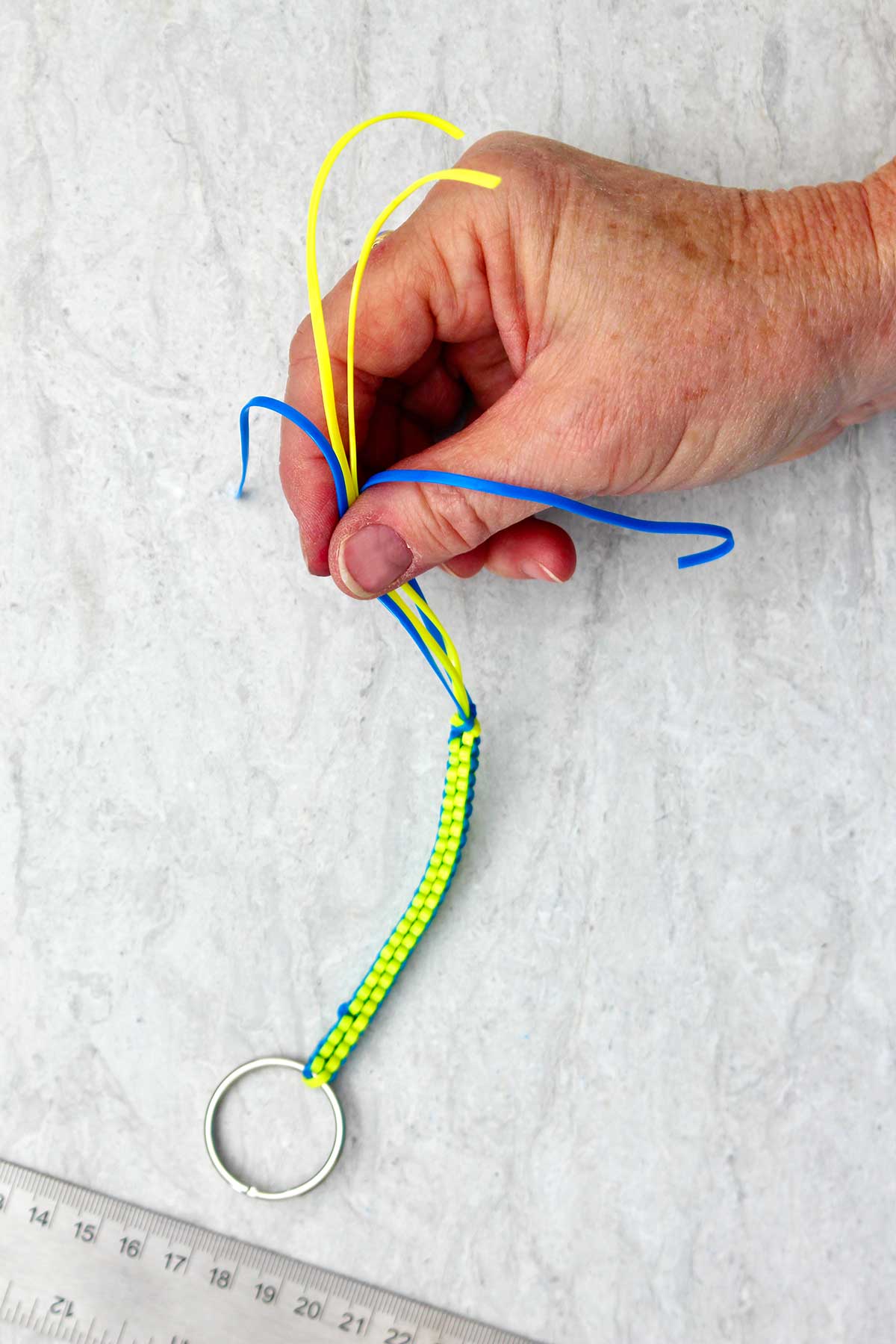 Chaveiro boondoggle azul e amarelo sendo segurado na ponta por uma mão.