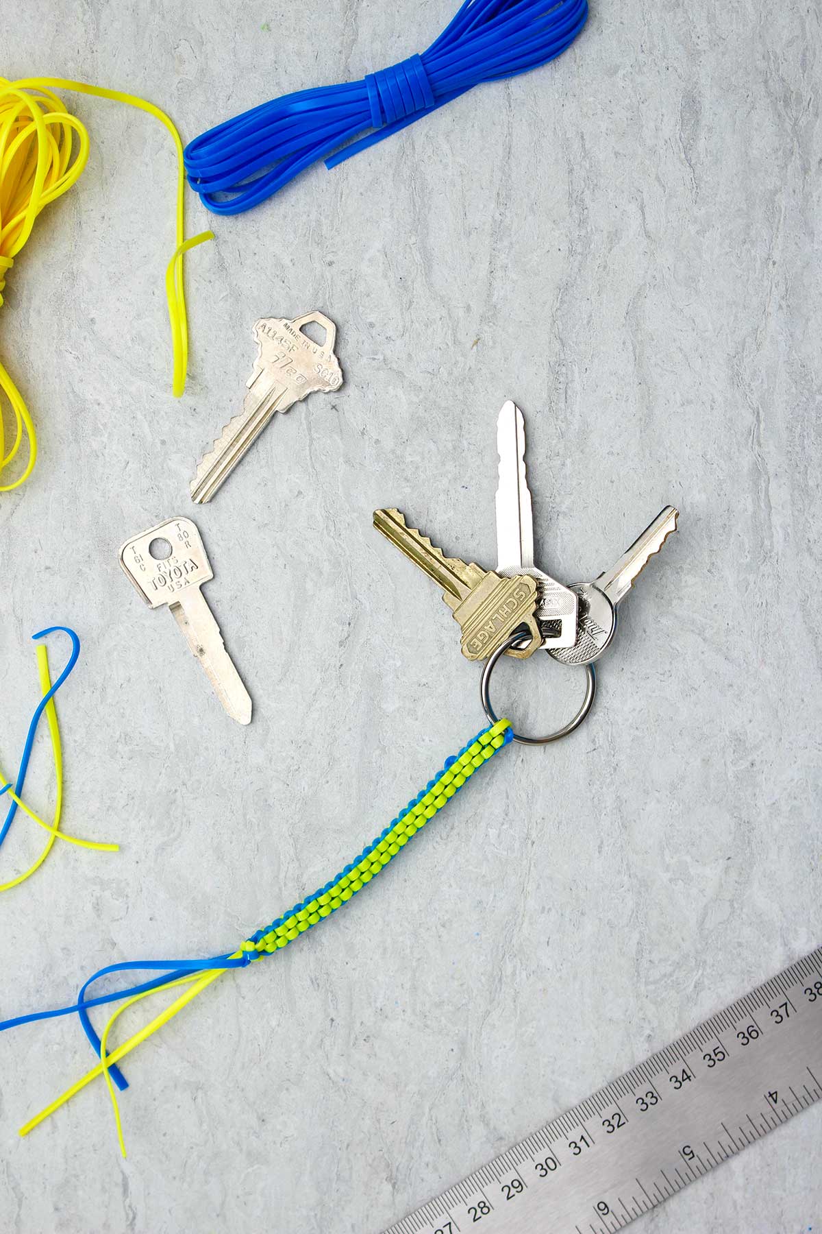 Um chaveiro boondoggle azul e amarelo completo com três chaves anexadas e materiais ao redor.