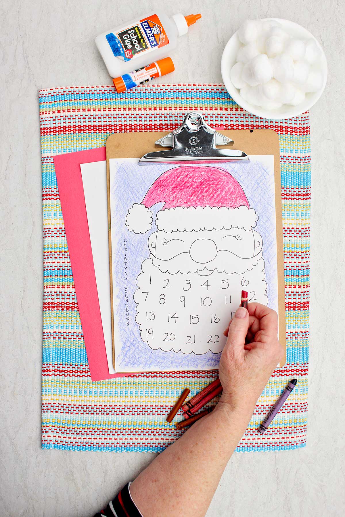Uma pessoa colorindo o chapéu do Papai Noel de vermelho na impressão do calendário.
