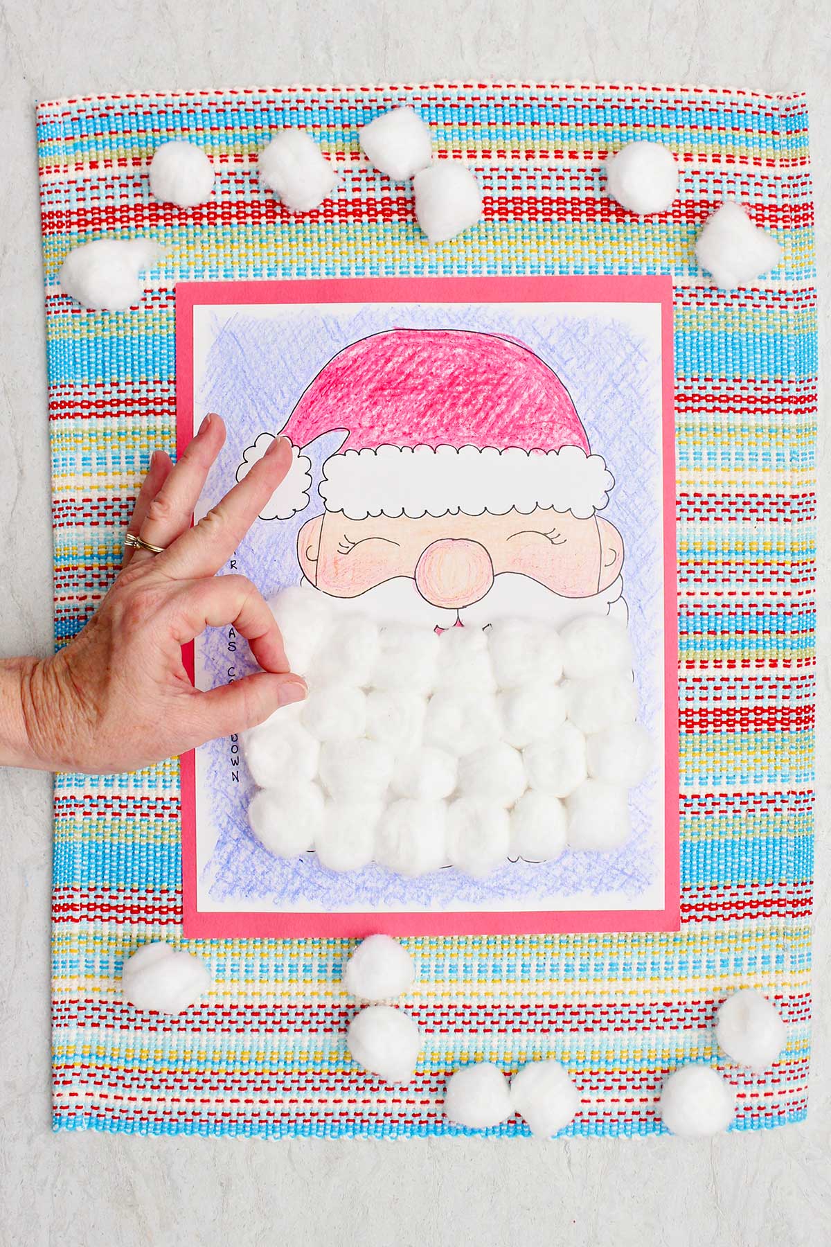 Um calendário de contagem regressiva de Natal completo, colorido com giz de cera e a barba do Papai Noel coberta com bolas de algodão e uma pessoa fazendo o sinal de "ok".