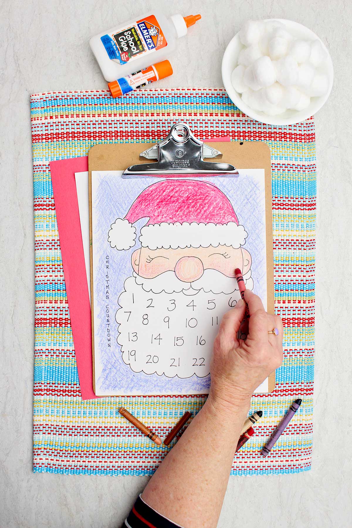 Uma pessoa colorindo as bochechas do Papai Noel de um tom rosado com um lápis de cor vermelho.