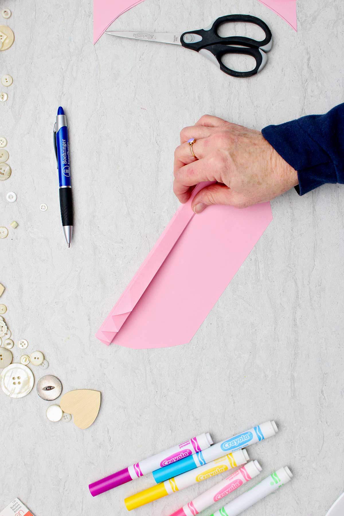 Pessoa dobrando um pedaço de papel rosa claro para fazer um coração de papel em acordeão.