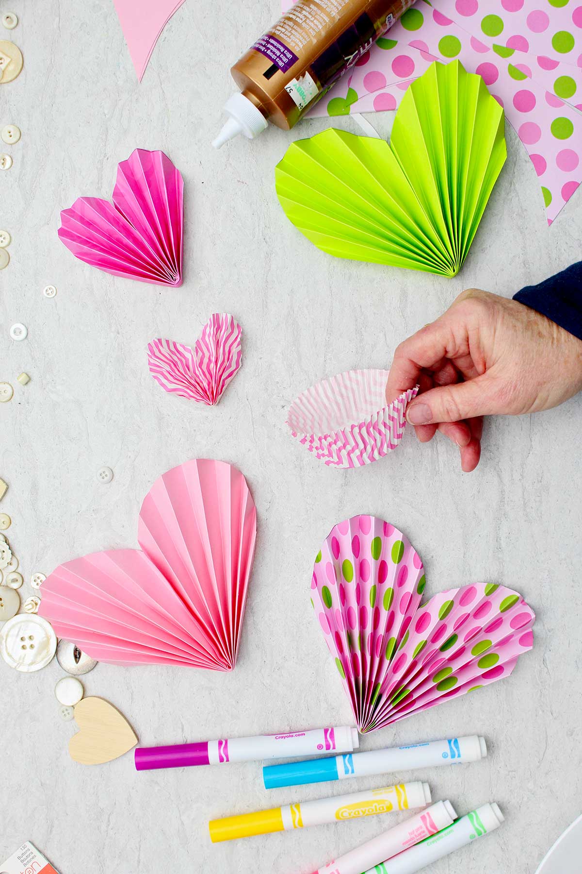 Pessoa segurando forminhas de cupcake rosa e brancas com outros corações em papel colorido ao redor.