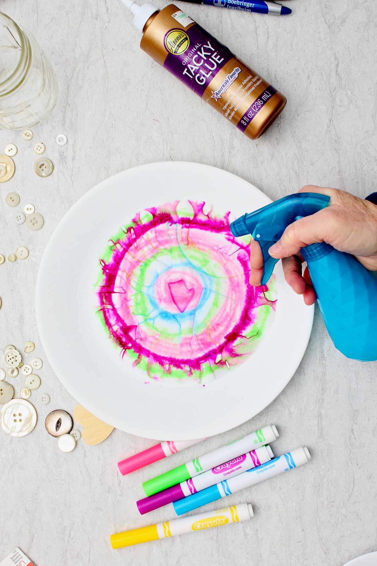 Pessoa borrifando água em um pedaço circular de papel para fazer um coração de papel acordeão tie-dye.