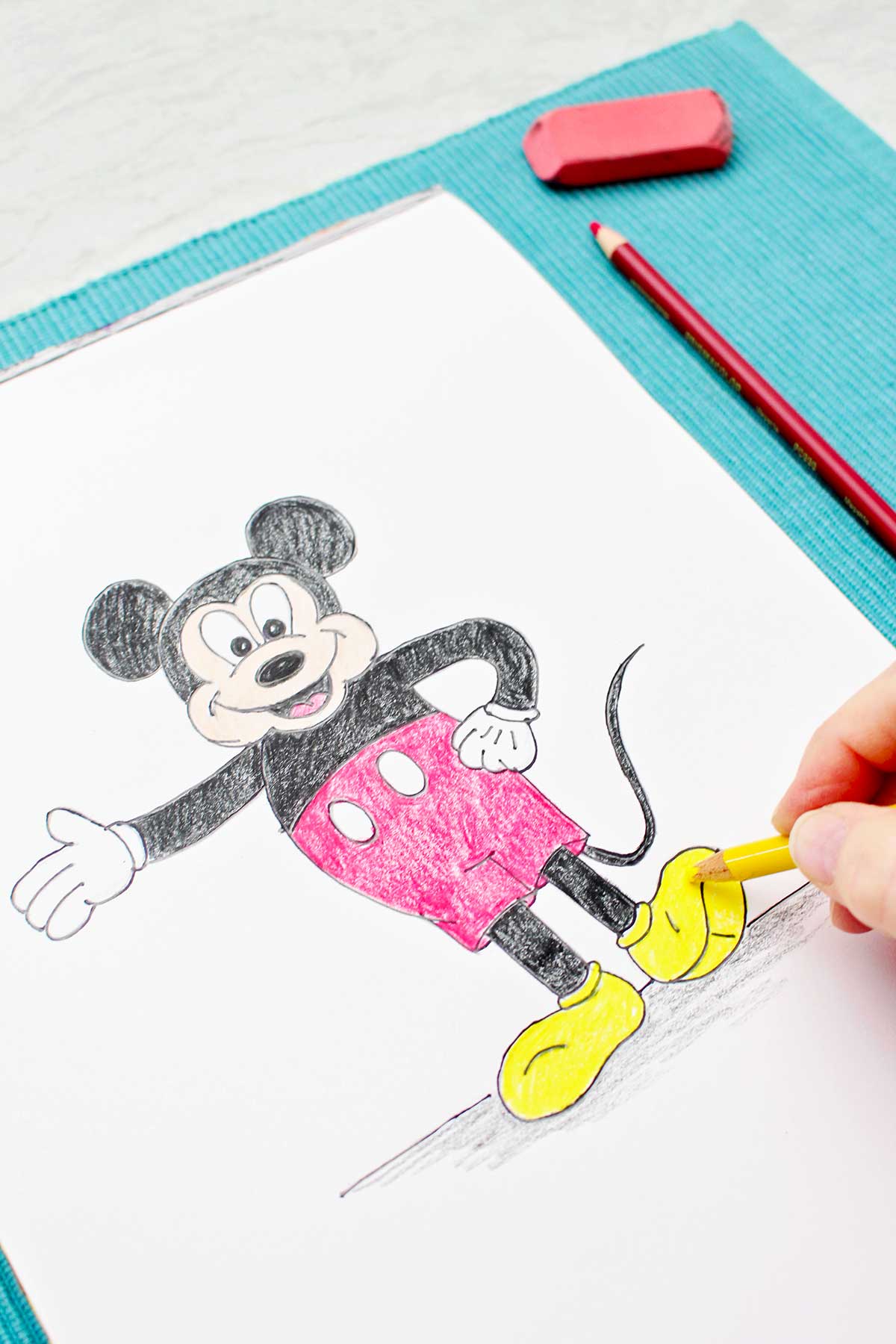 Uma pessoa colorindo os sapatos do Mickey com um lápis de cor amarelo.