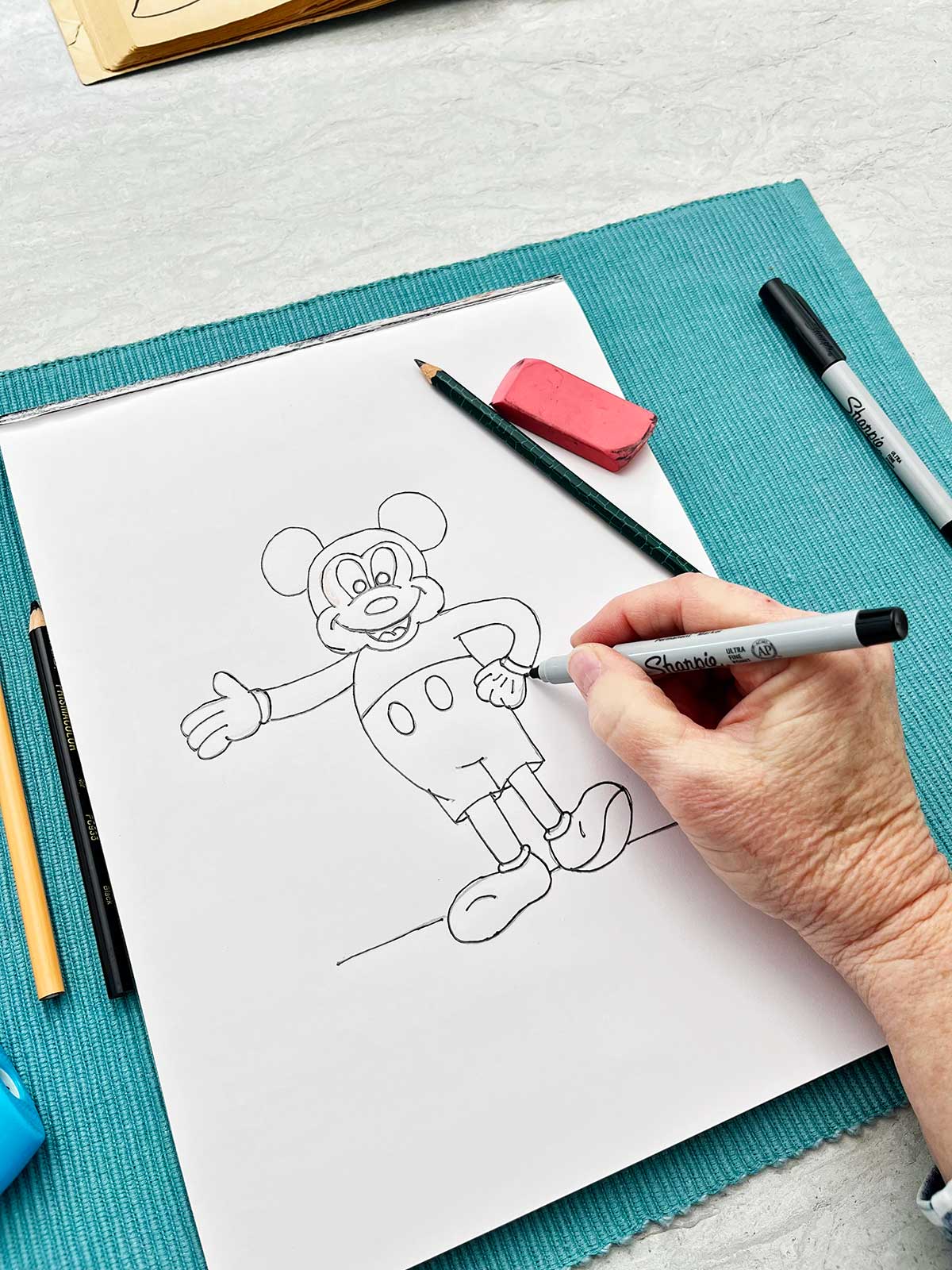Uma pessoa revisando o esboço a lápis do Mickey Mouse com um marcador sharpie.