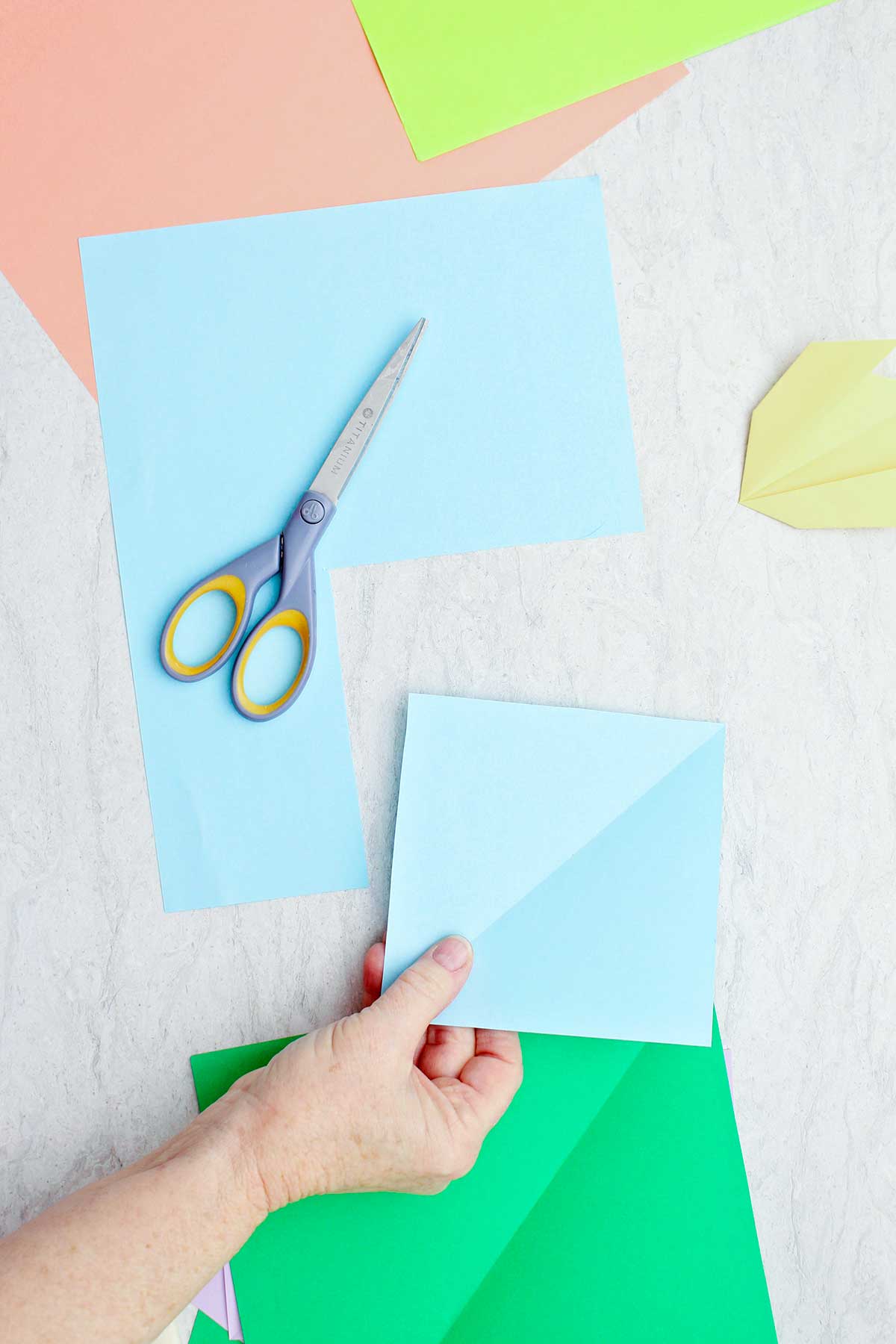 Uma pessoa cortando um quadrado de papel azul claro para fazer uma flor de origami.