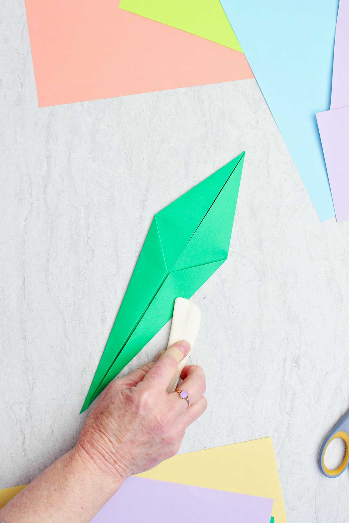 Uma pessoa usando uma espátula de osso para vincar um papel verde para fazer um caule.