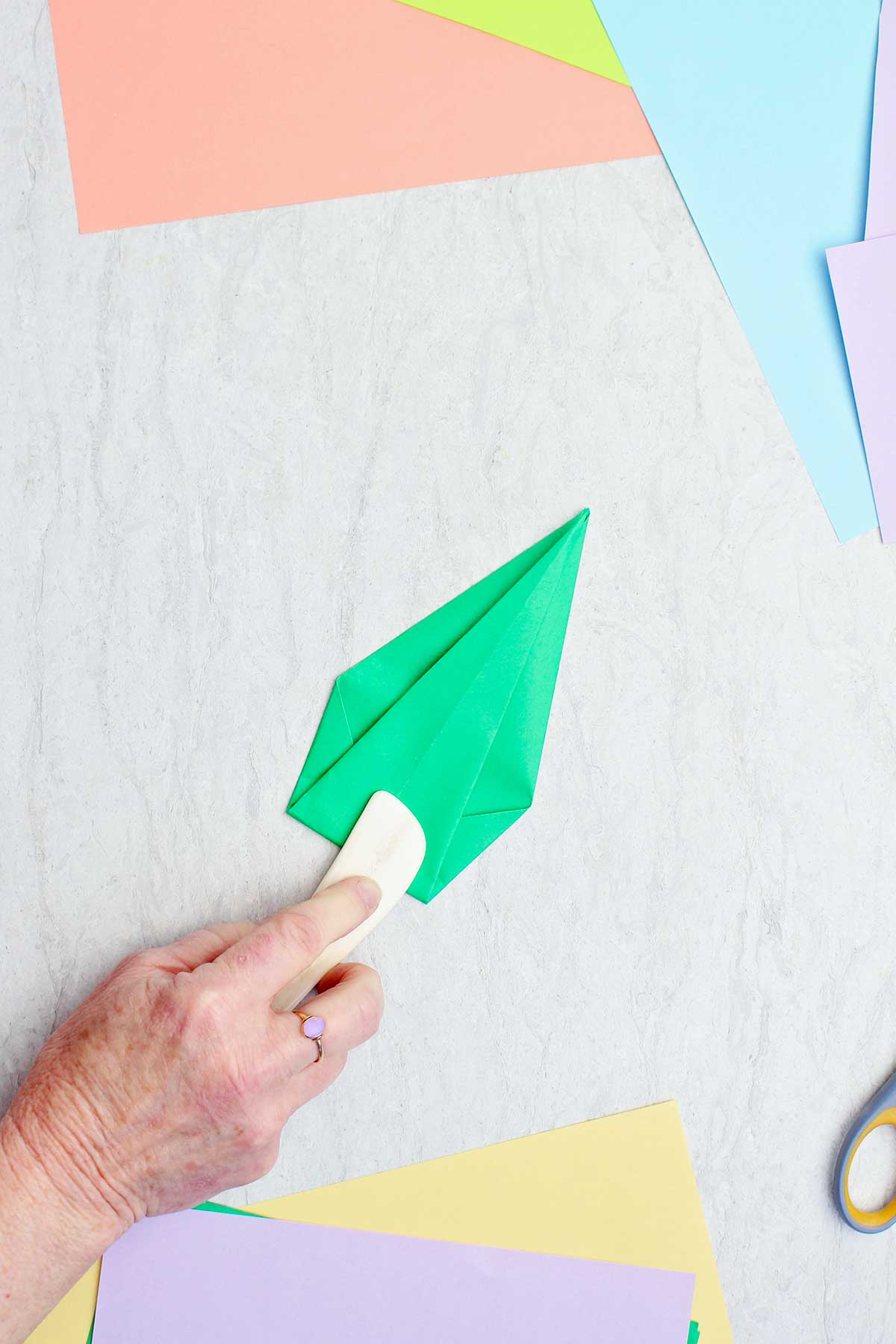 Uma pessoa usando uma espátula de osso para vincar um papel verde para fazer um caule.