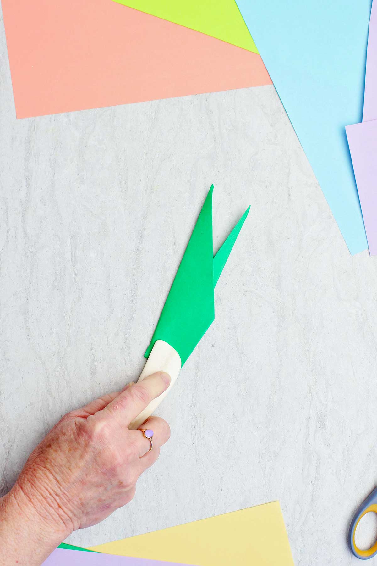 Uma pessoa usando uma espátula de osso para vincar um papel verde para fazer um caule.