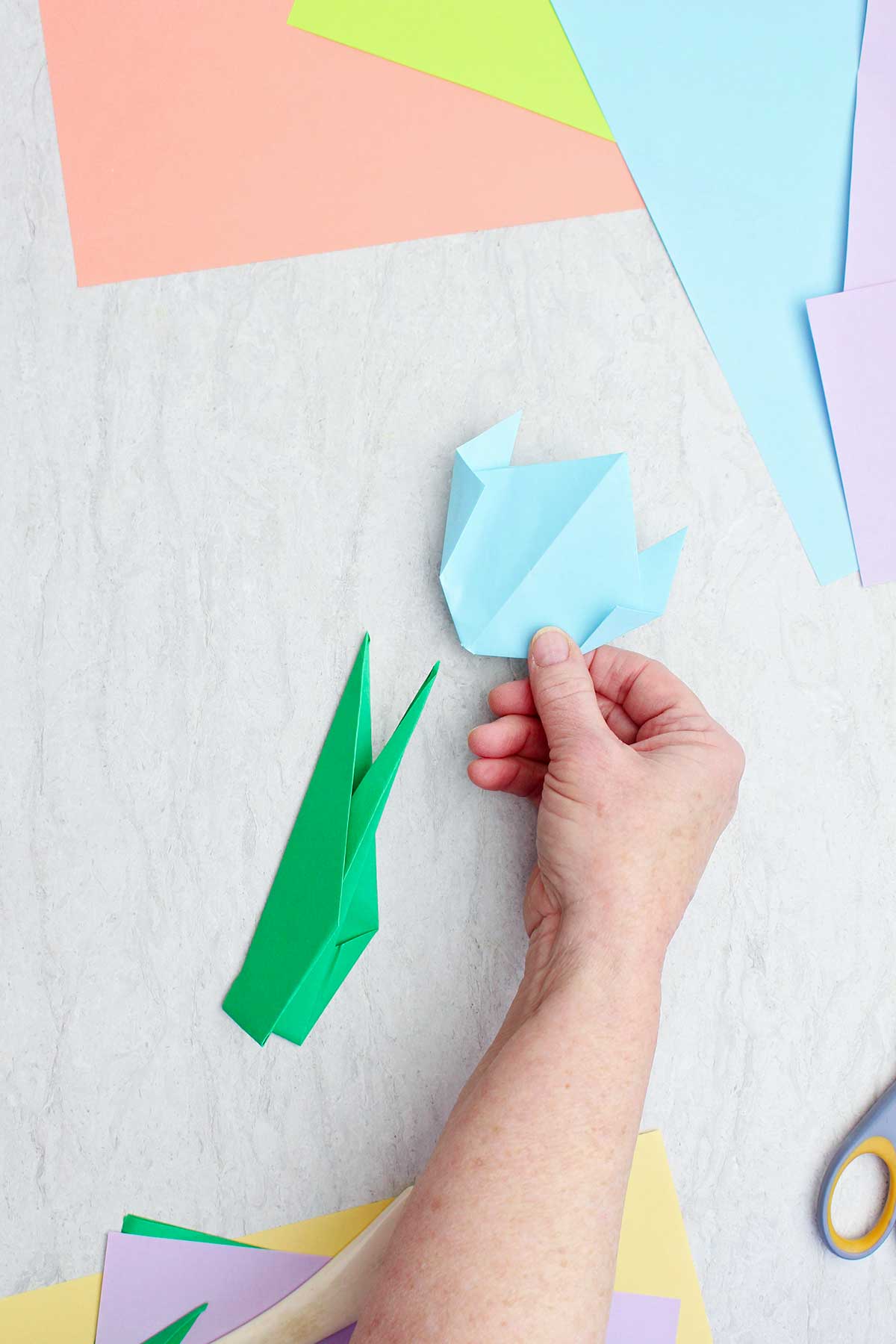 Uma pessoa colocando uma flor de origami azul claro sobre um caule de origami.