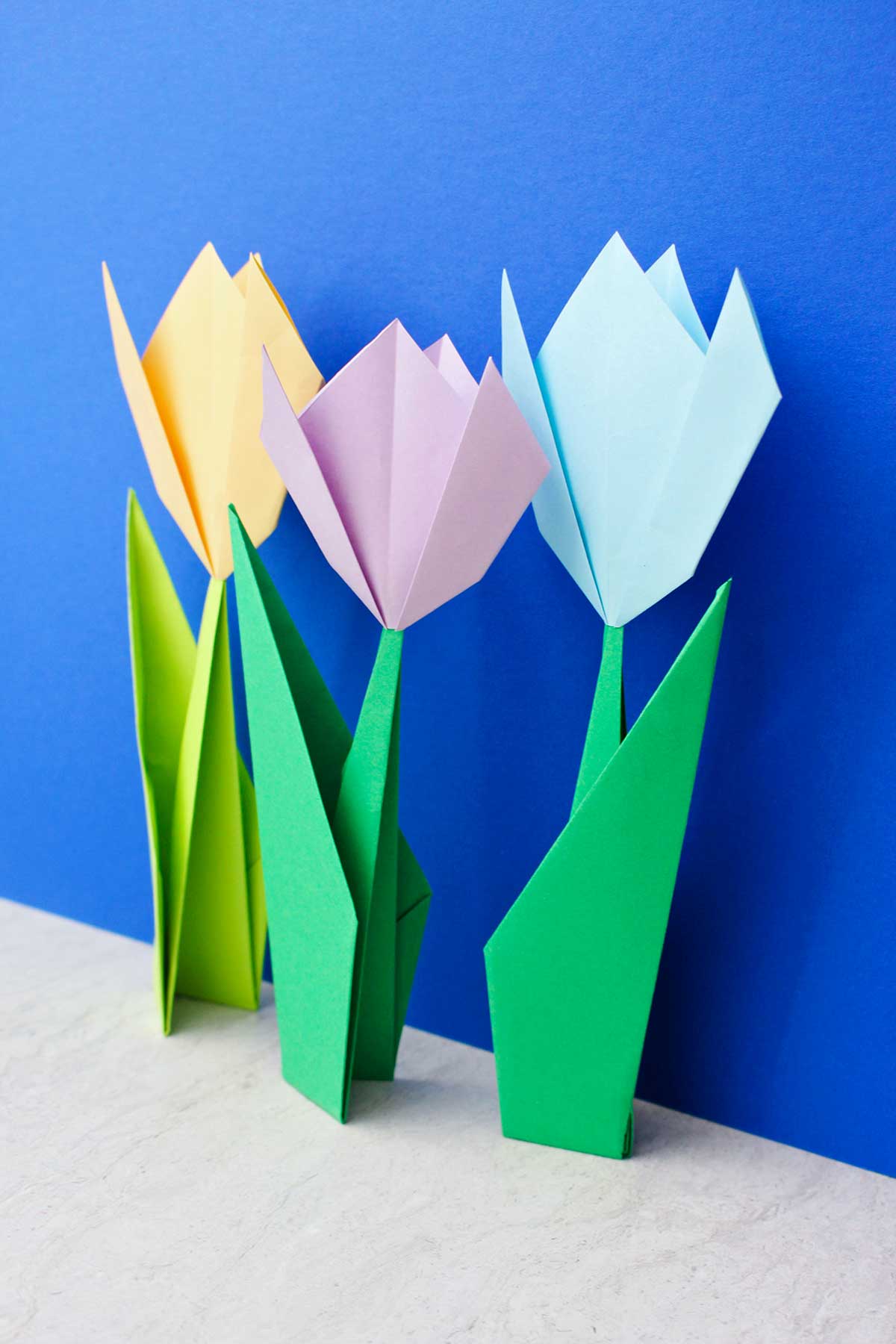 Três flores de origami em pé diante de um fundo azul brilhante.