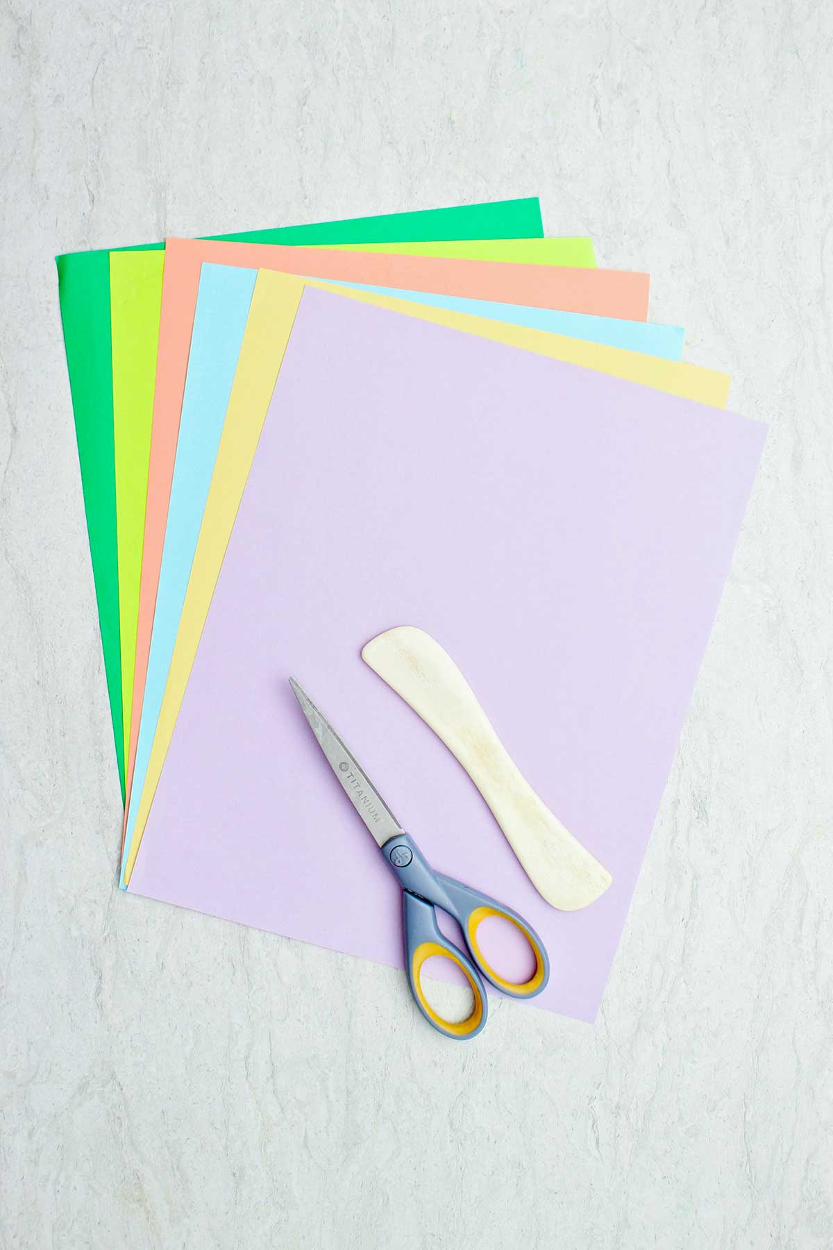 Papel colorido, uma espátula de madeira e tesouras.