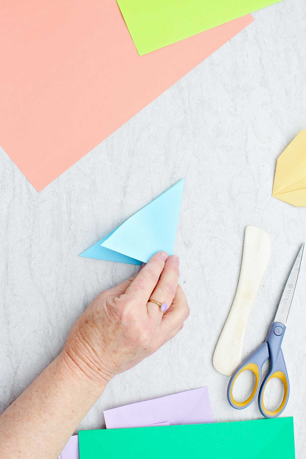 Uma pessoa dobrando um pedaço de papel azul claro para fazer uma flor.