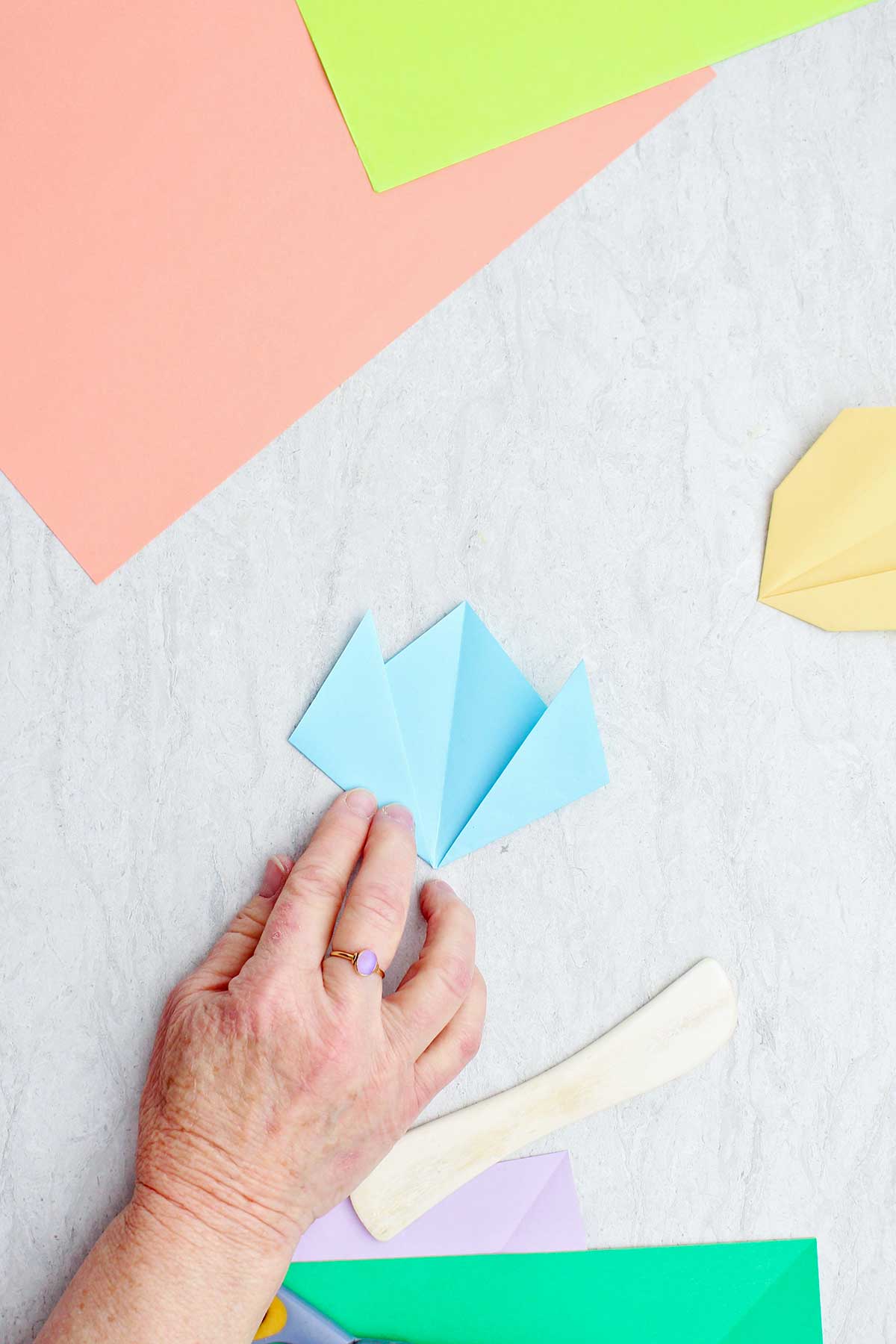 Uma pessoa dobrando um pedaço de papel azul claro para fazer uma flor.