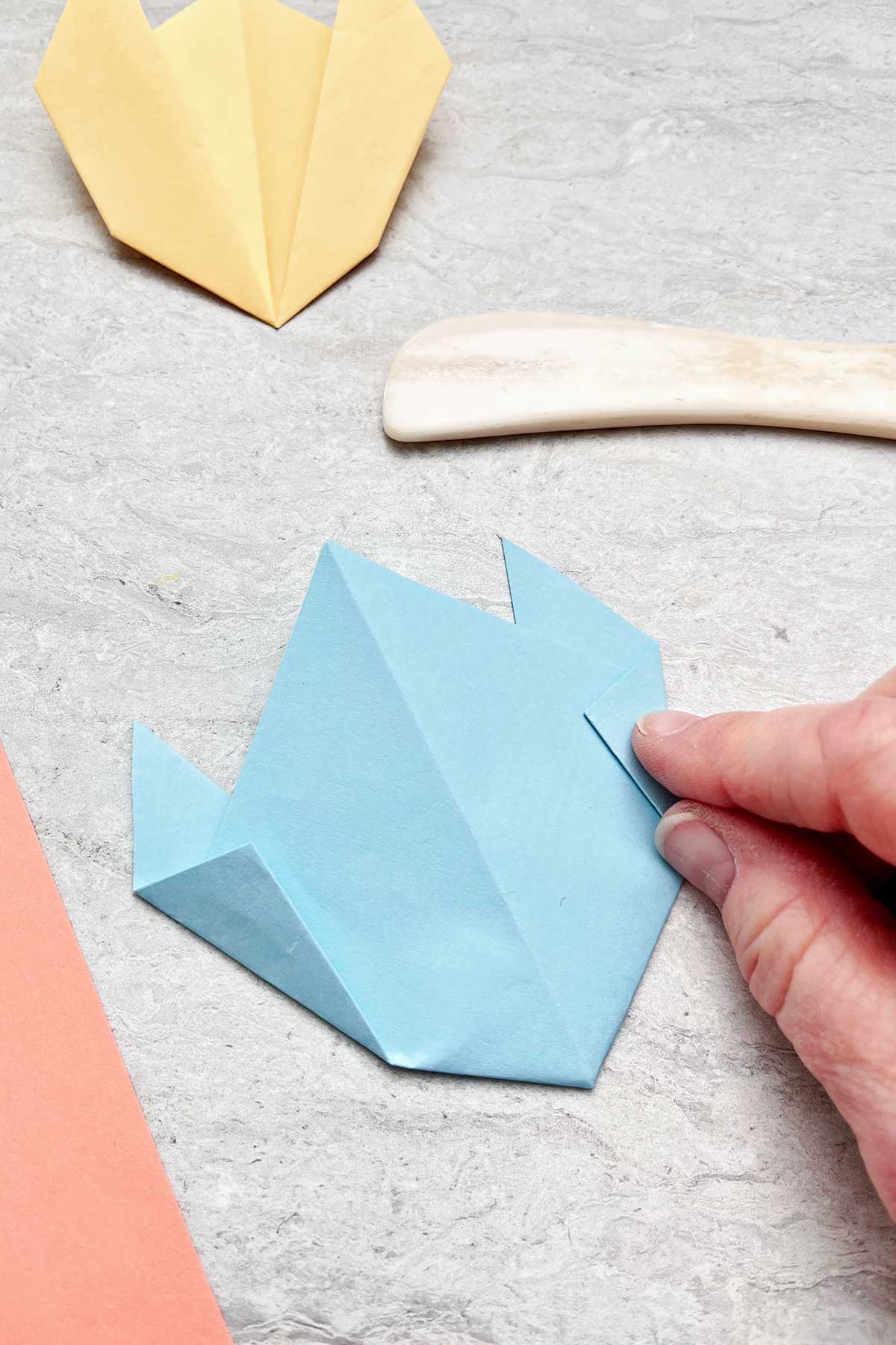 Uma pessoa dobrando um pedaço de papel azul claro para fazer uma flor.