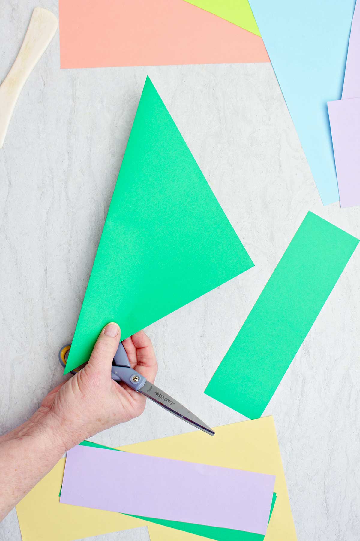 Uma pessoa cortando um pedaço de papel verde para fazer um caule de flor de origami.