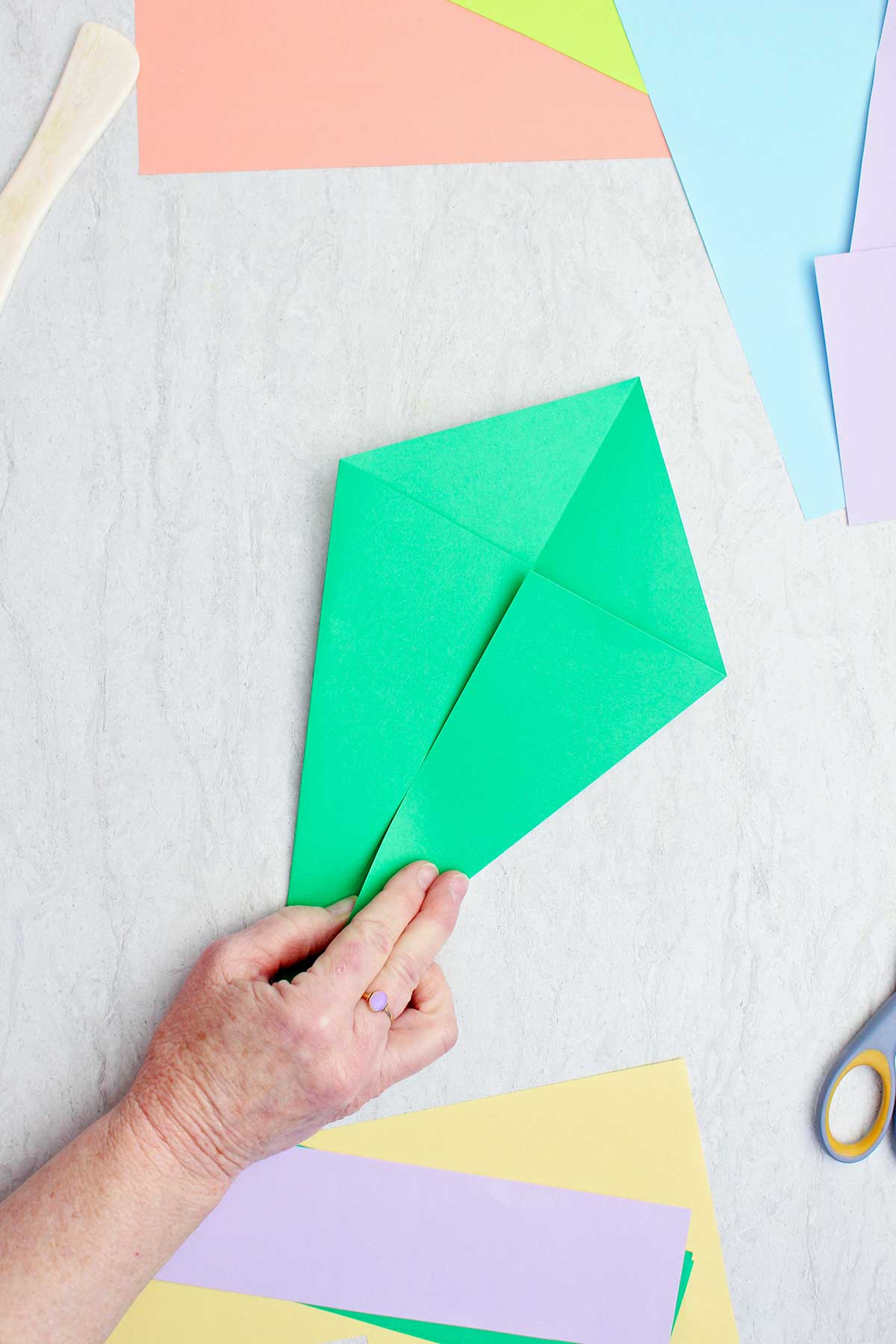 Uma pessoa dobrando um pedaço de papel verde para fazer um caule de origami.