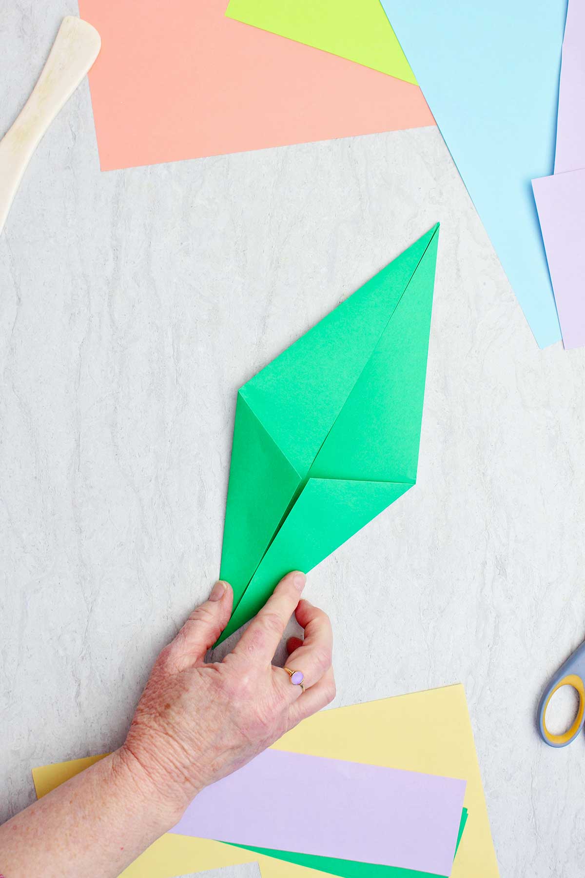 Uma pessoa dobrando um pedaço de papel verde para fazer um caule de origami.