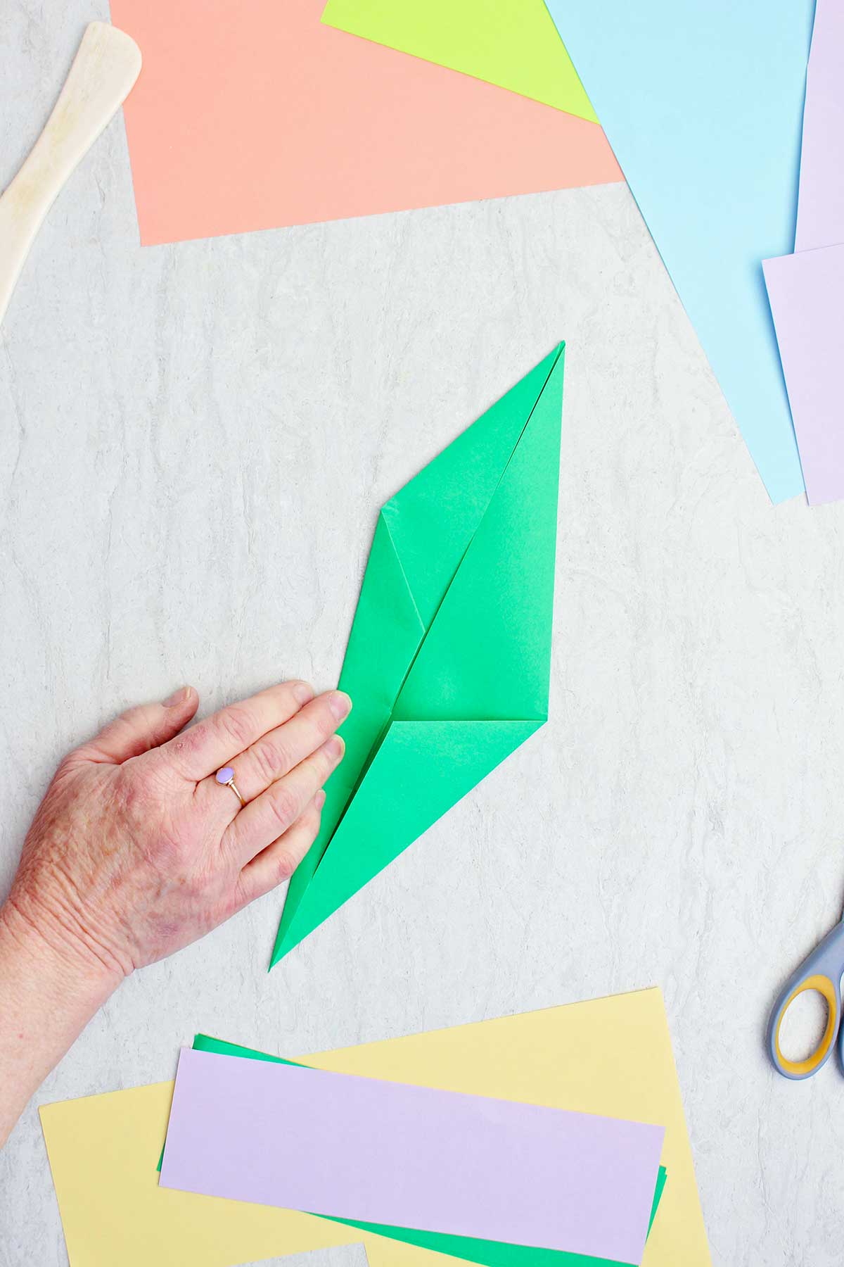 Uma pessoa dobrando um pedaço de papel verde para fazer um caule de origami.
