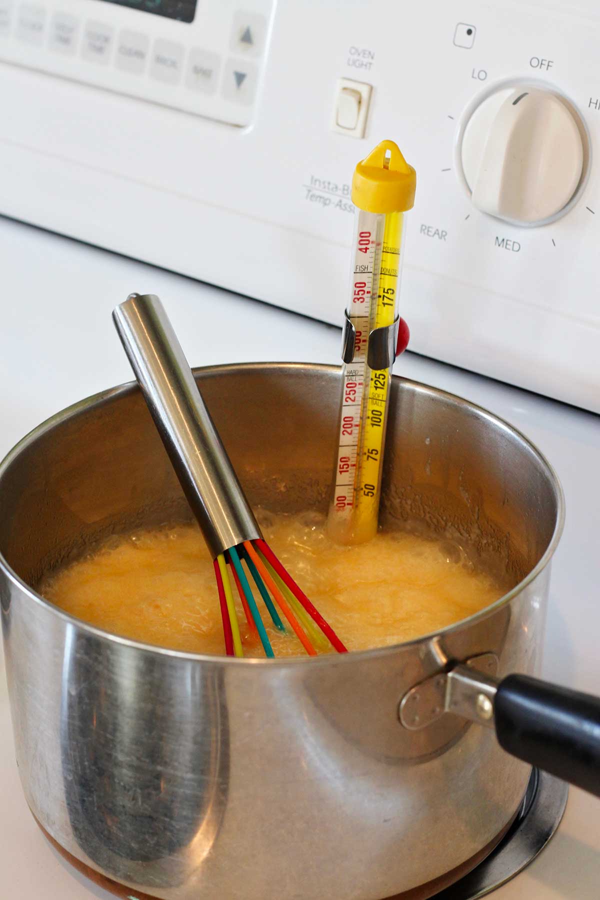 Mistura de fudge fervendo no fogão com um termômetro de doces medindo a temperatura.