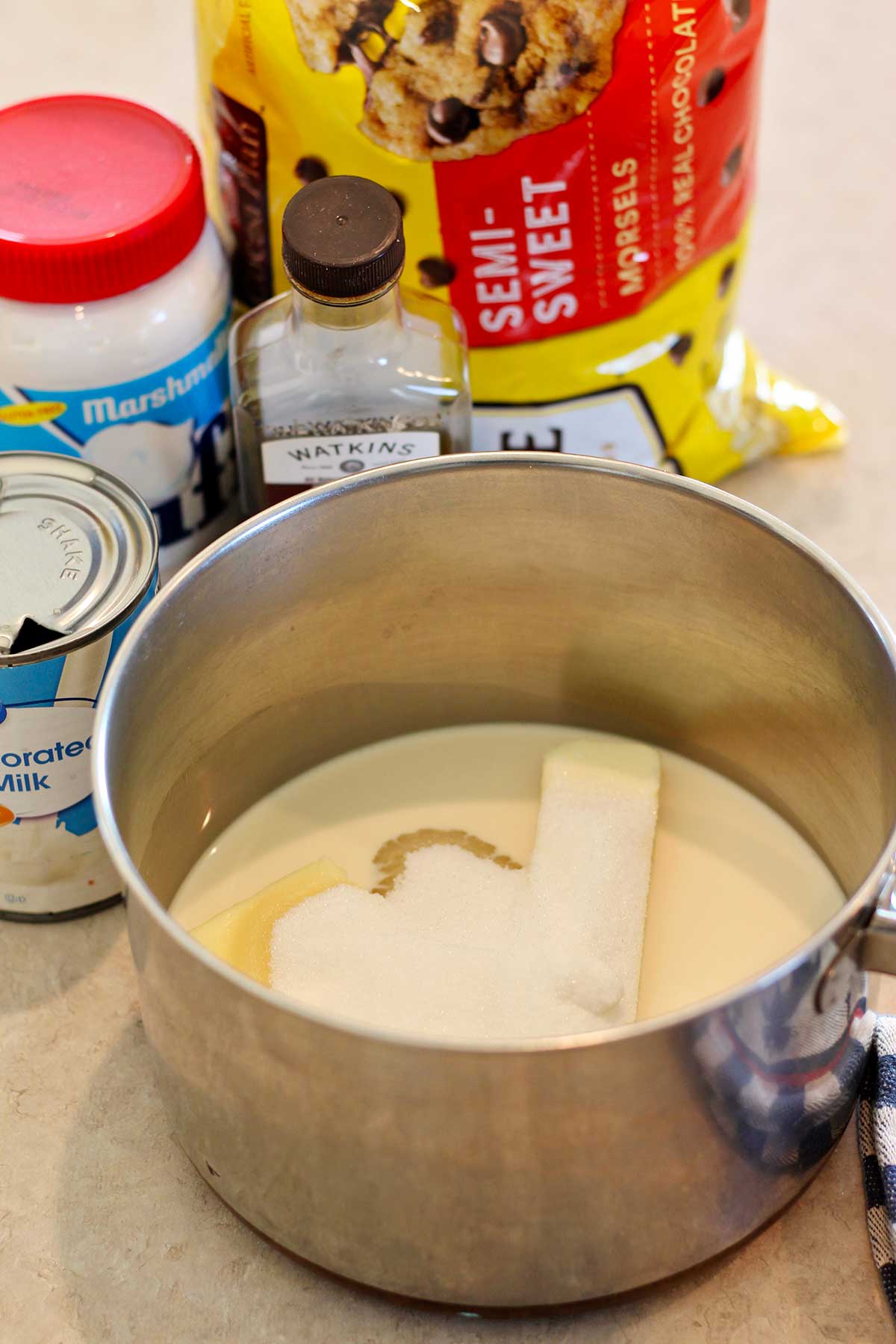 Uma panela cheia de leite evaporado, manteiga e açúcar com outros ingredientes ao fundo.