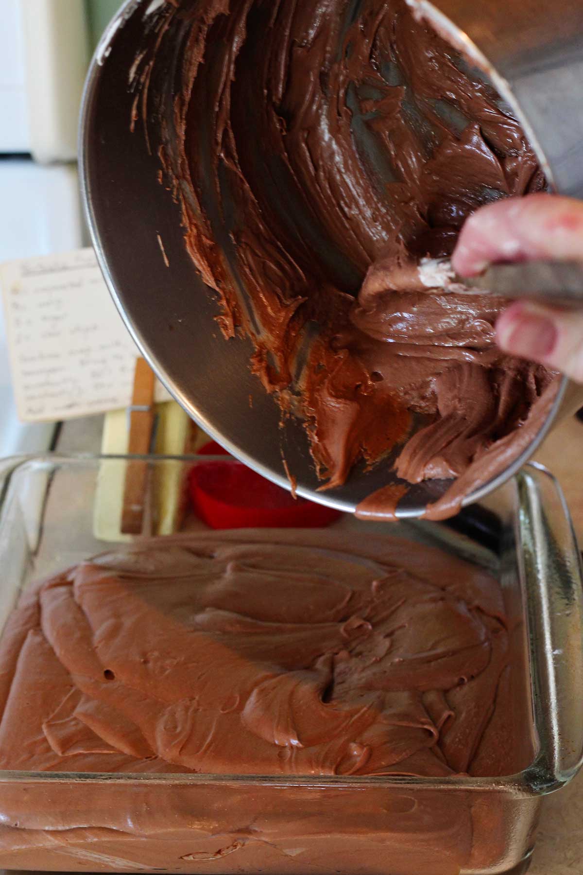 Pessoa retirando a mistura de fudge da panela para a forma de vidro.