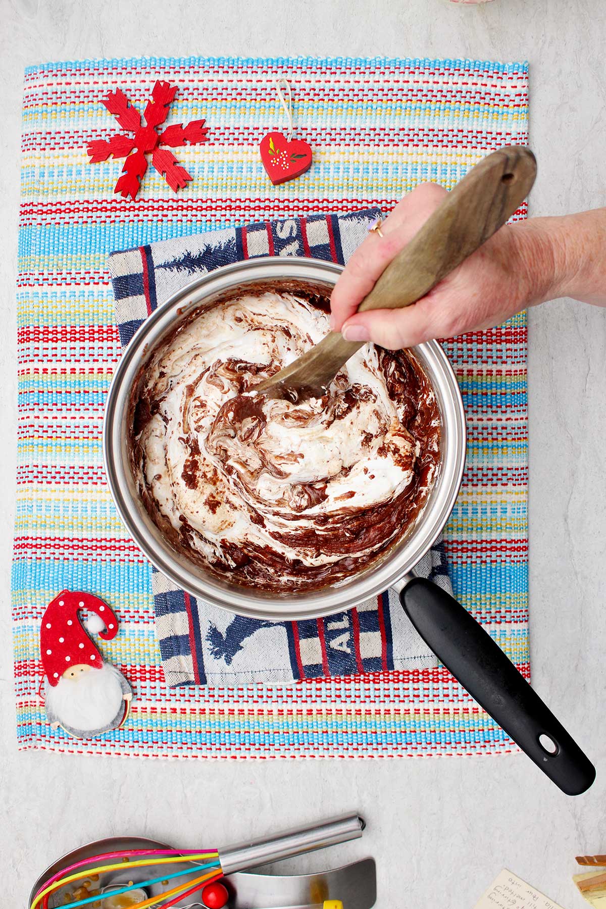 Uma pessoa mexendo a mistura de fluff e fudge de chocolate fora do fogo em um jogo americano colorido.