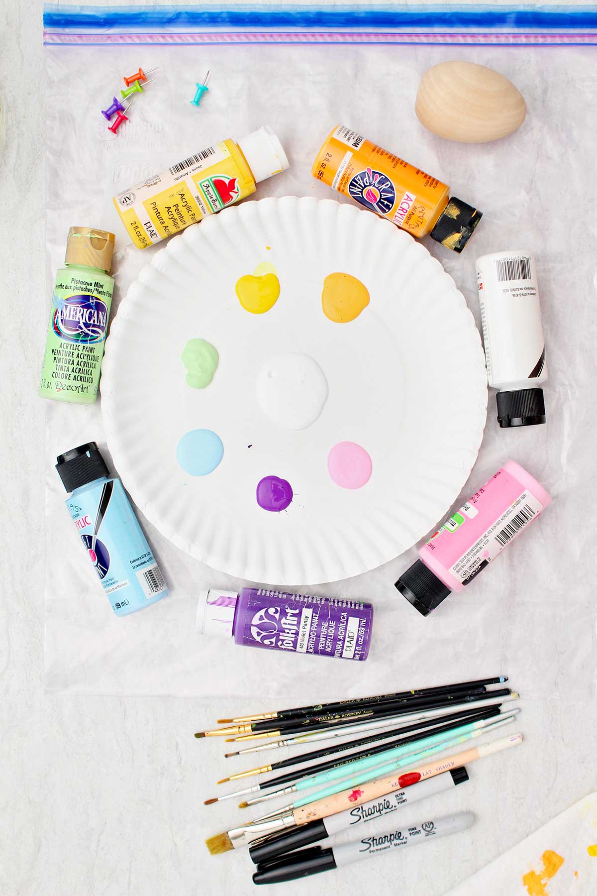 Um prato de papel com diferentes cores de tinta acrílica, pincéis e tintas acrílicas.