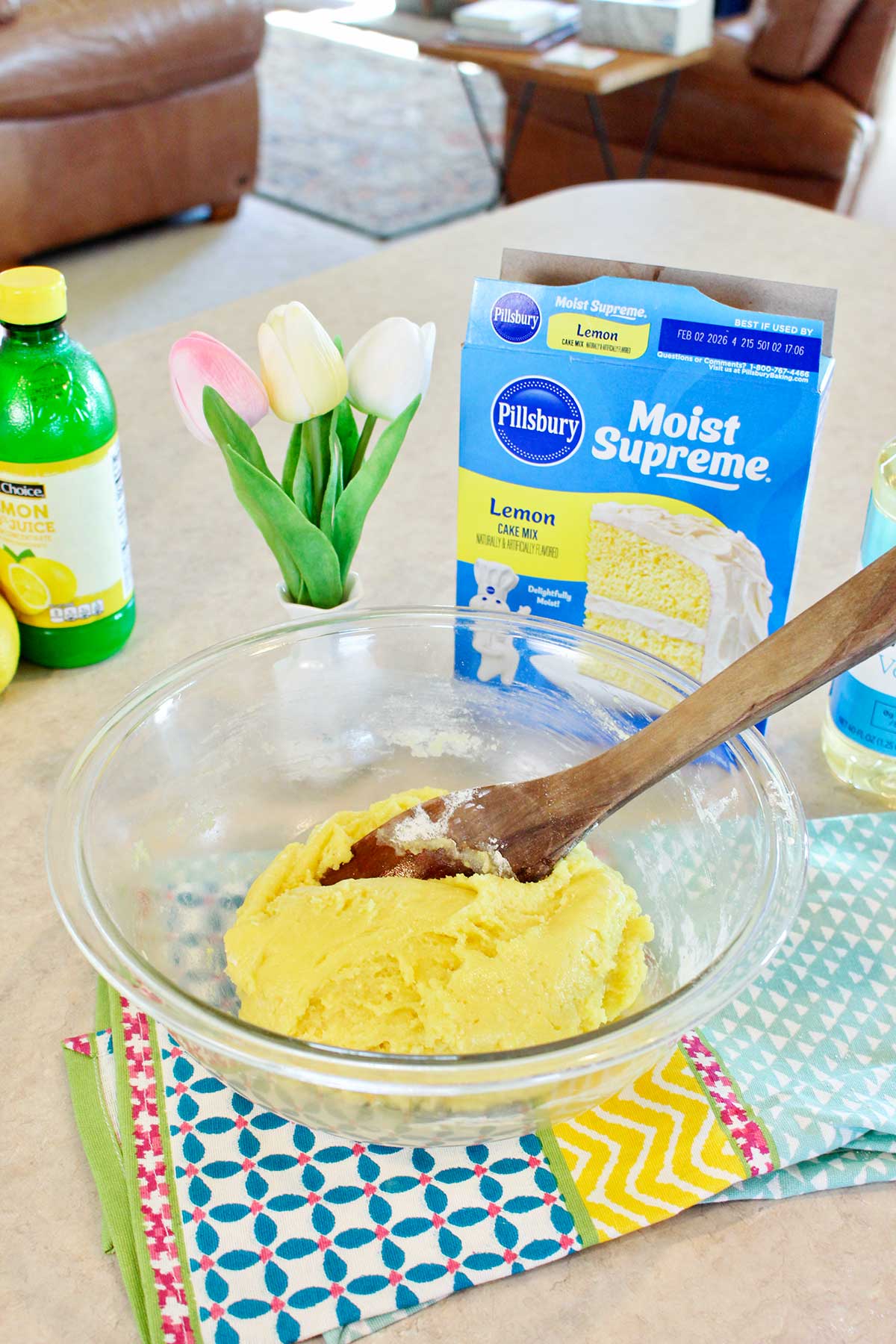 Massa de bolo de limão misturada em uma tigela com ingredientes e tulipas ao fundo.
