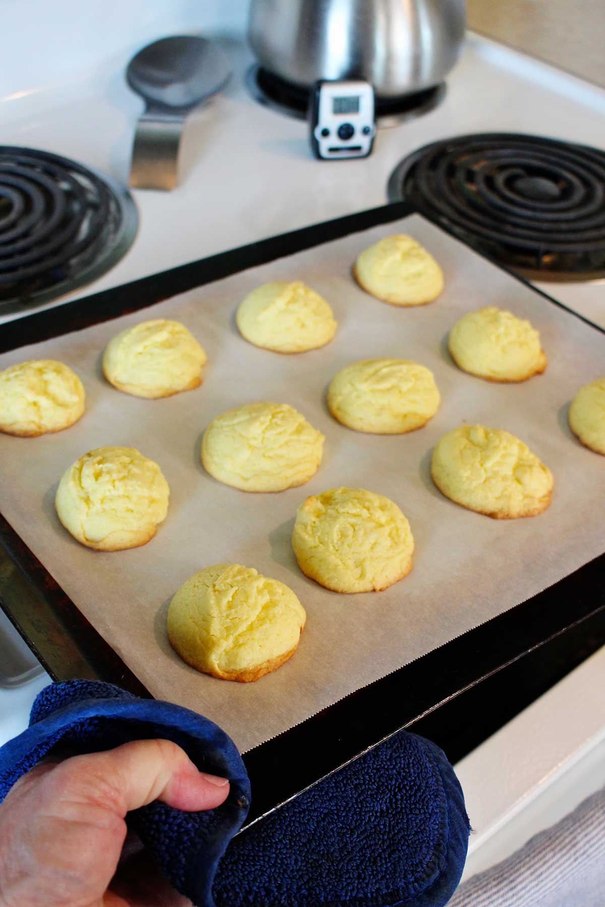Uma pessoa retirando uma assadeira com biscoitos de bolo de limão assados do forno.