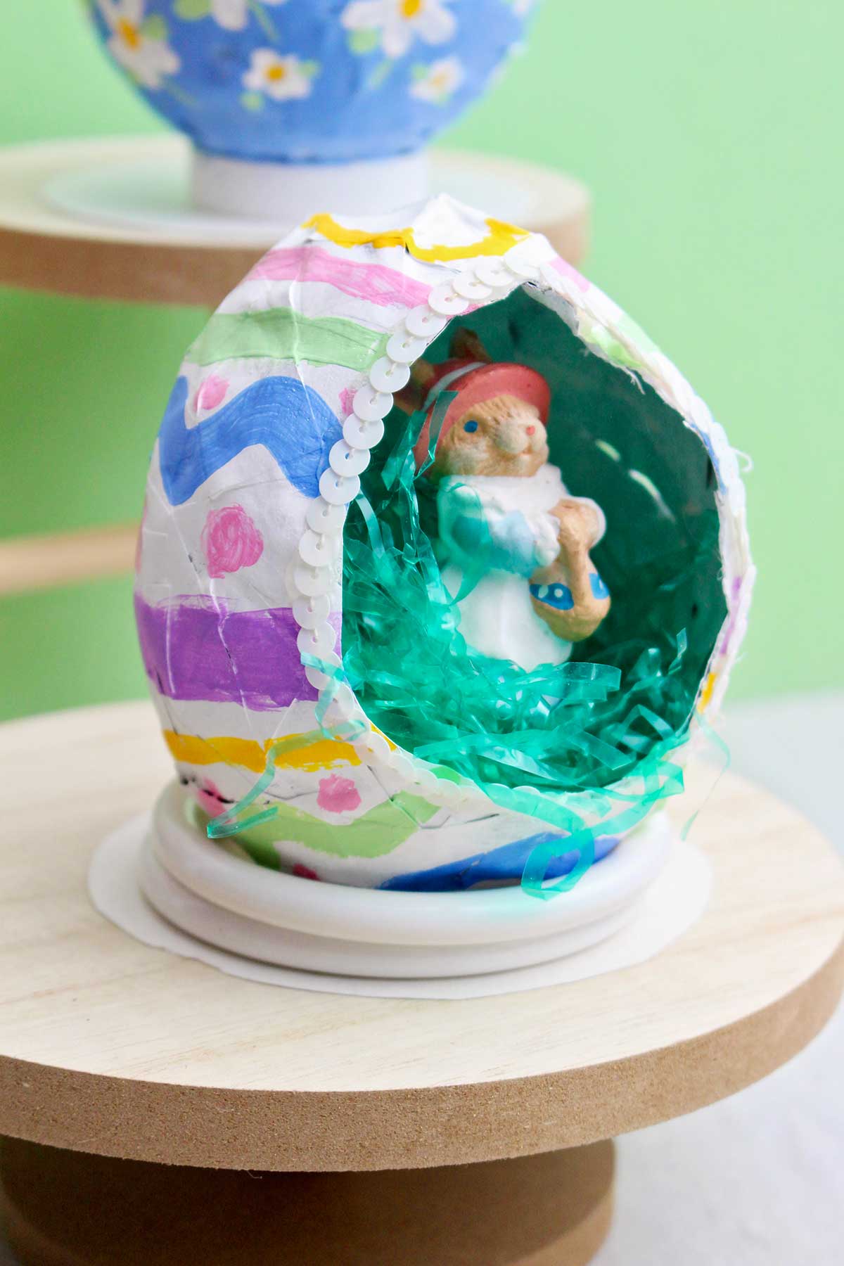 Um projeto de papel machê de ovo de Páscoa esvaziado com um pequeno coelho dentro.