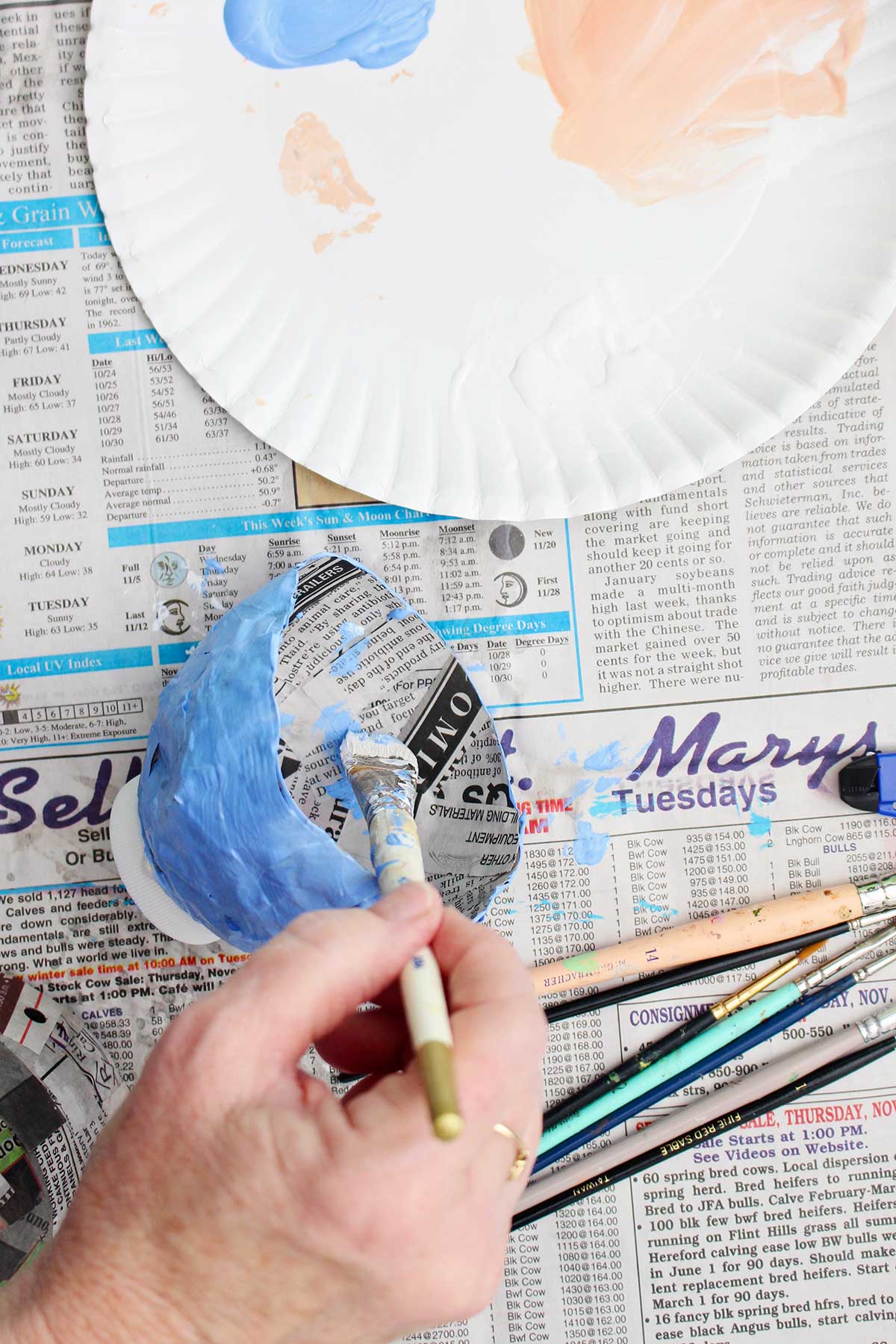 Uma pessoa pintando o interior do seu projeto de papel machê seco de azul claro.