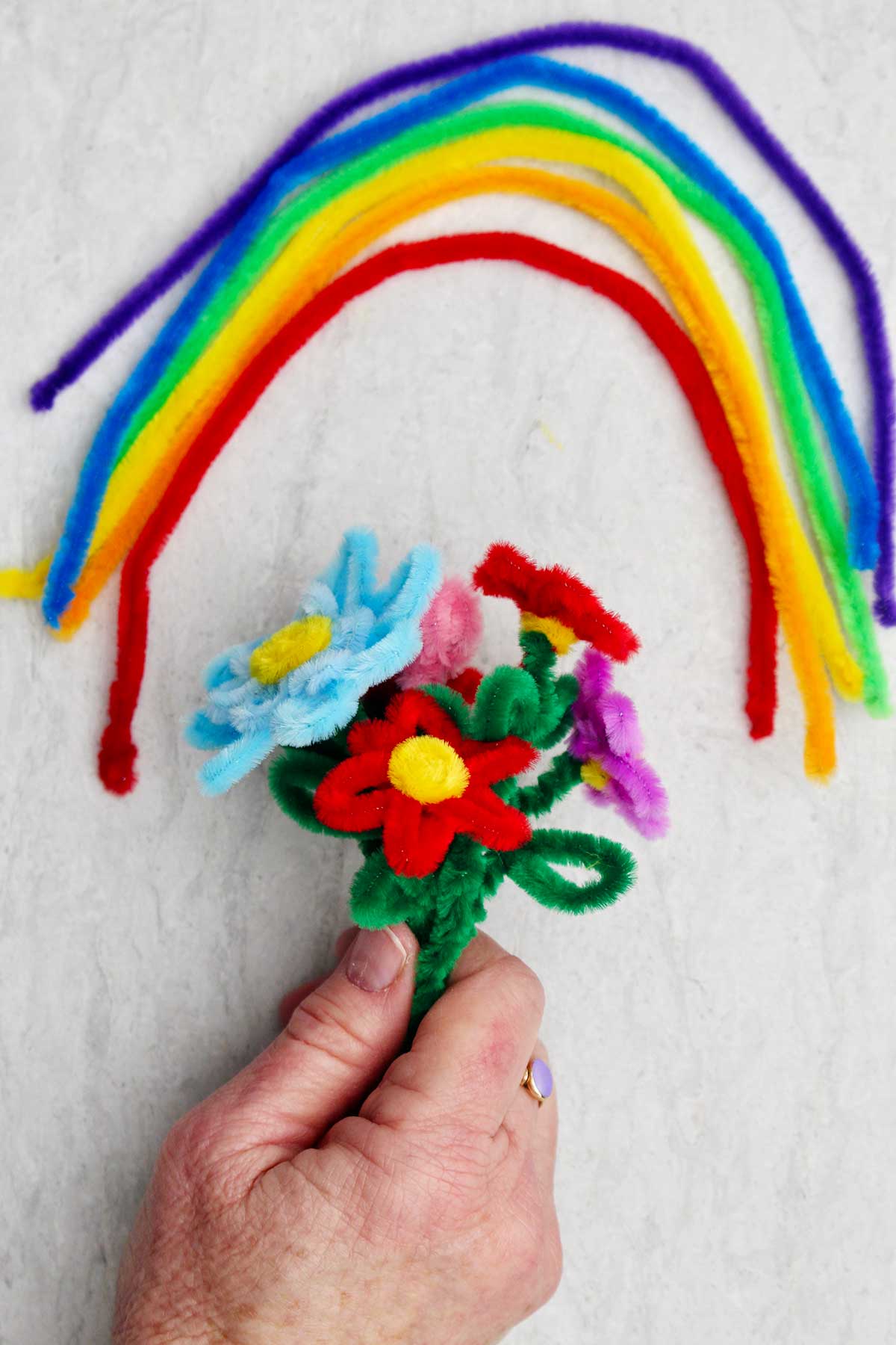 Uma pessoa segurando um buquê de flores de limpadores de pipe de várias cores com um arco-íris de limpadores de pipe acima.