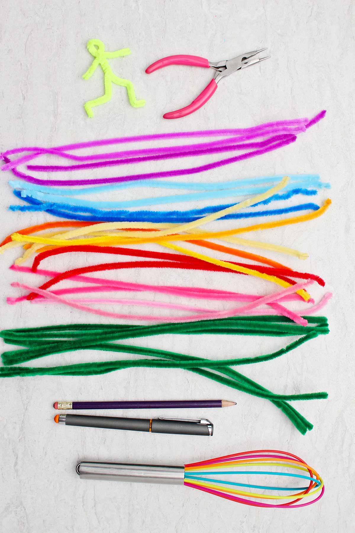 Um conjunto de limpadores de pipe coloridos, um batedor multicolorido, uma caneta, um lápis e alicates de bico fino.