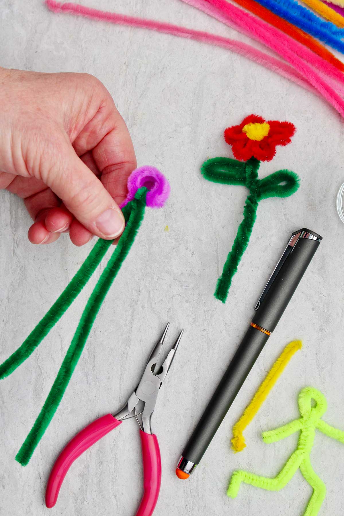 Uma pessoa segurando o início de uma flor de limpador de pipe com caule verde e outros suprimentos por perto.