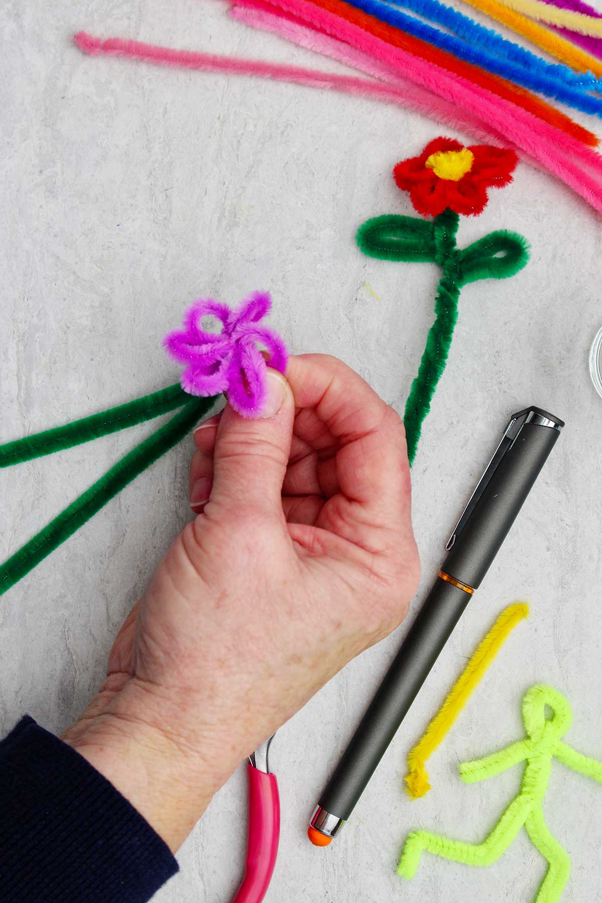 Pessoa segurando a flor de limpador de pipe enquanto cria as pétalas roxas.