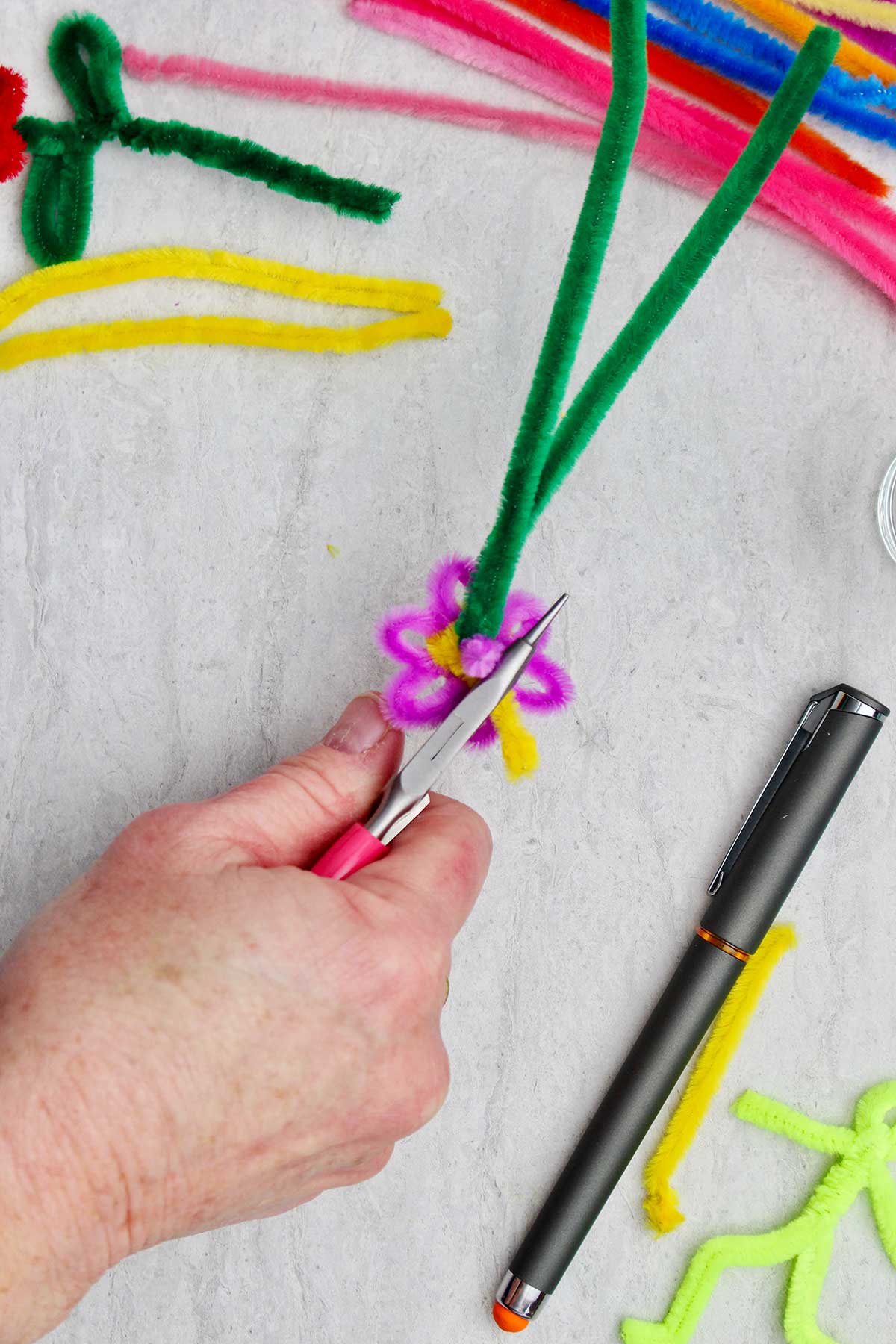 Uma pessoa dobrando e aparando o excesso de limpador de pipe amarelo na parte de trás da flor.