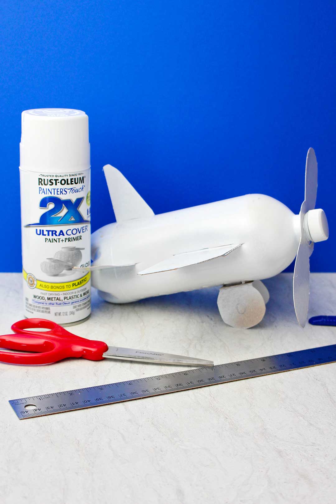 Avião de garrafa post pintado com spray branco contra fundo azul.
