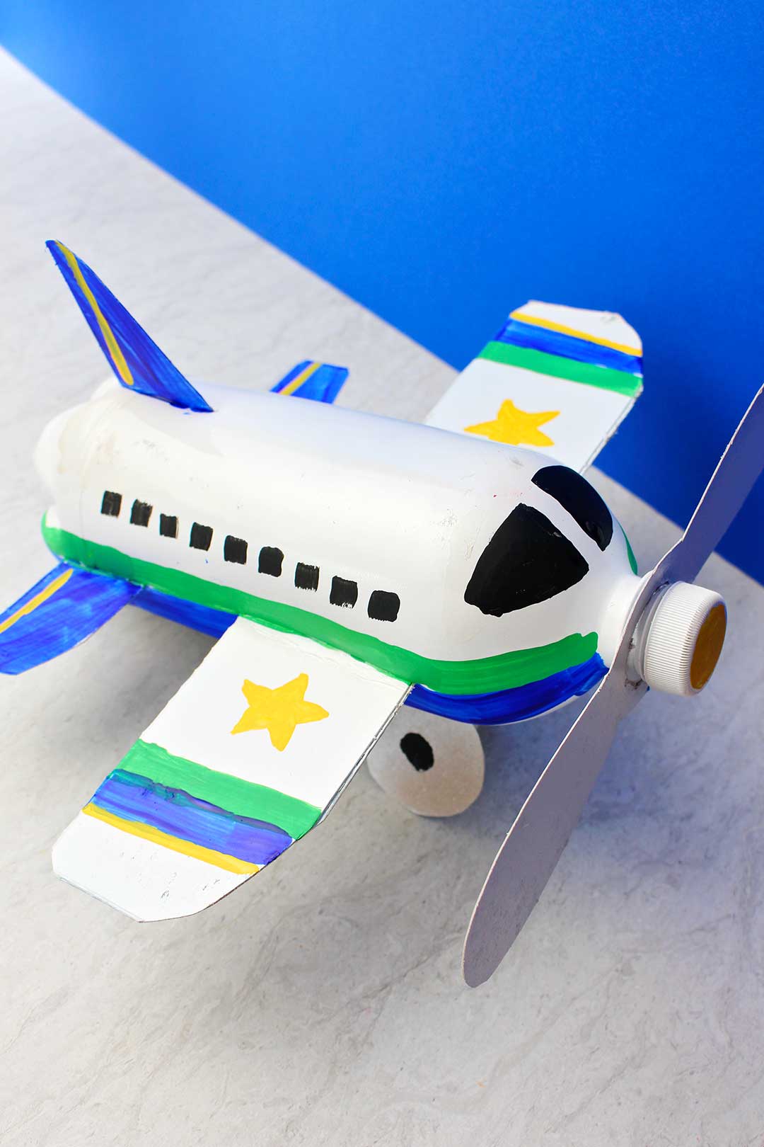 Vista de cima de um projeto de avião feito de garrafa completamente pintado e finalizado contra um fundo azul.