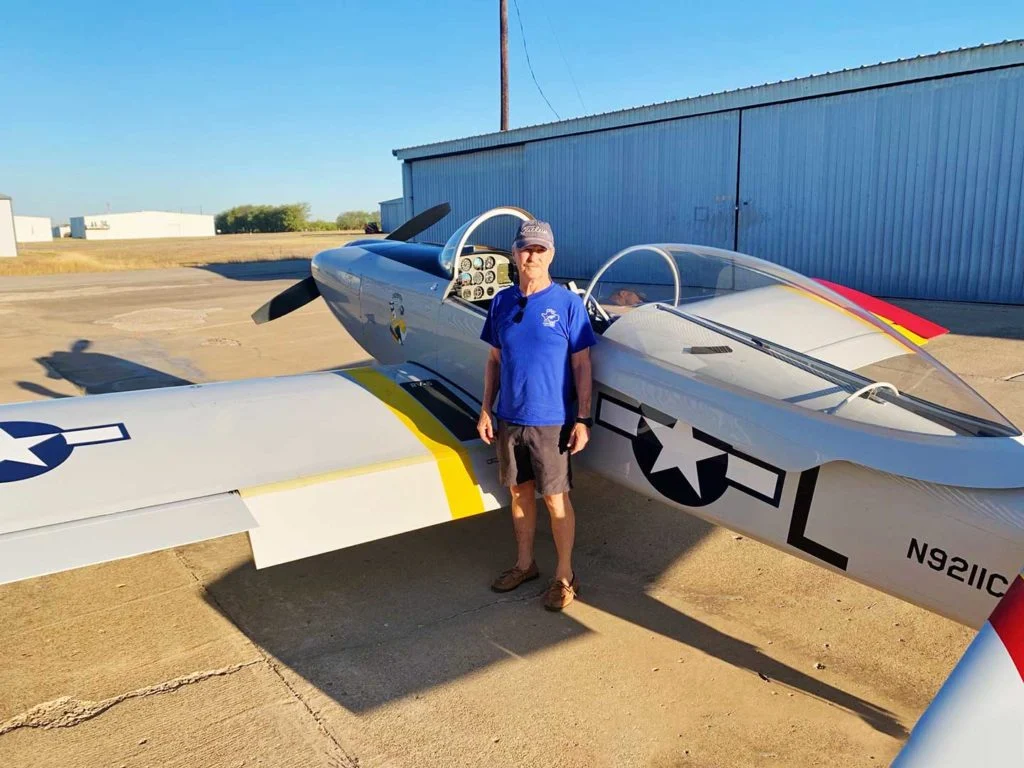 Homem vestindo camisa azul em frente a um pequeno avião de um passageiro do lado de fora.