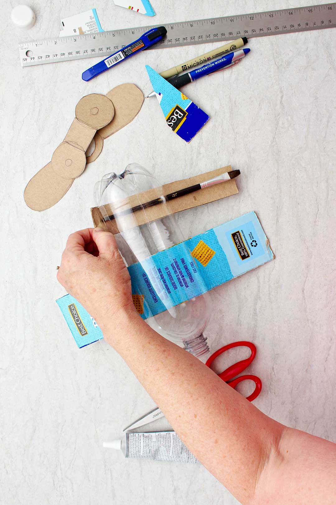 Mão puxando retângulo de papelão (asas) através de fenda na garrafa.