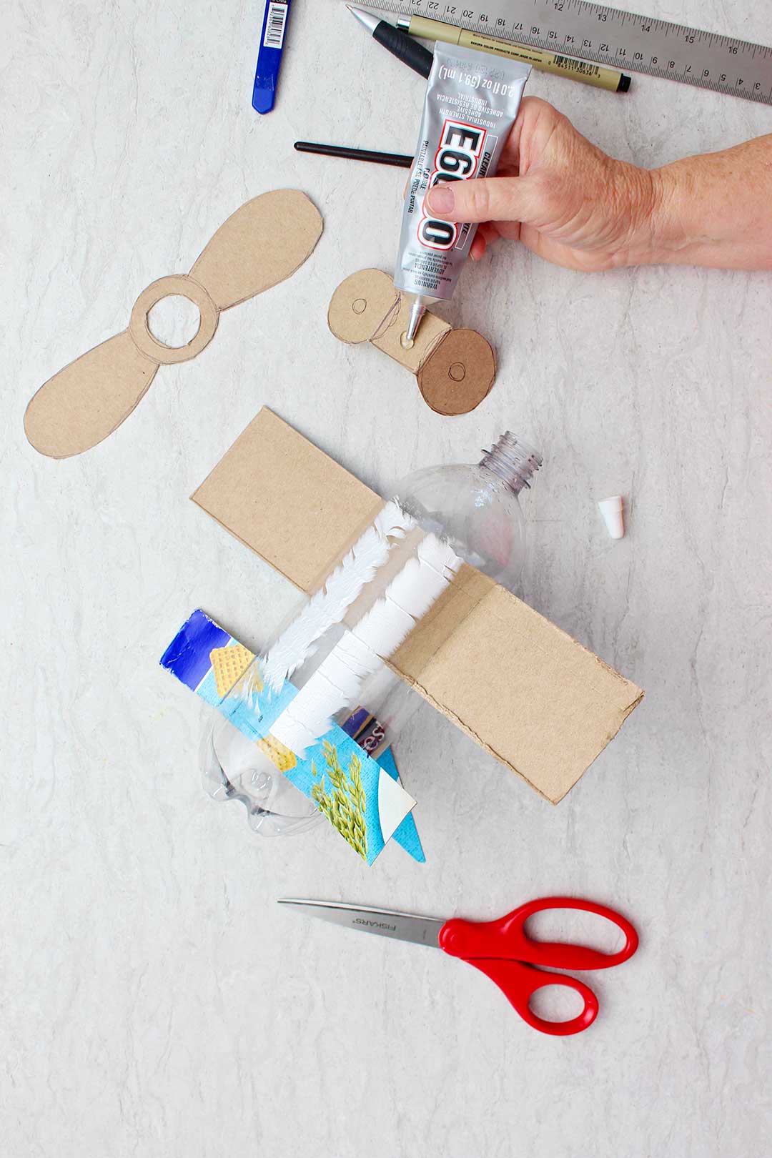 Mão colando peças de papelão cortadas para se assemelhar a rodas na parte inferior da garrafa.