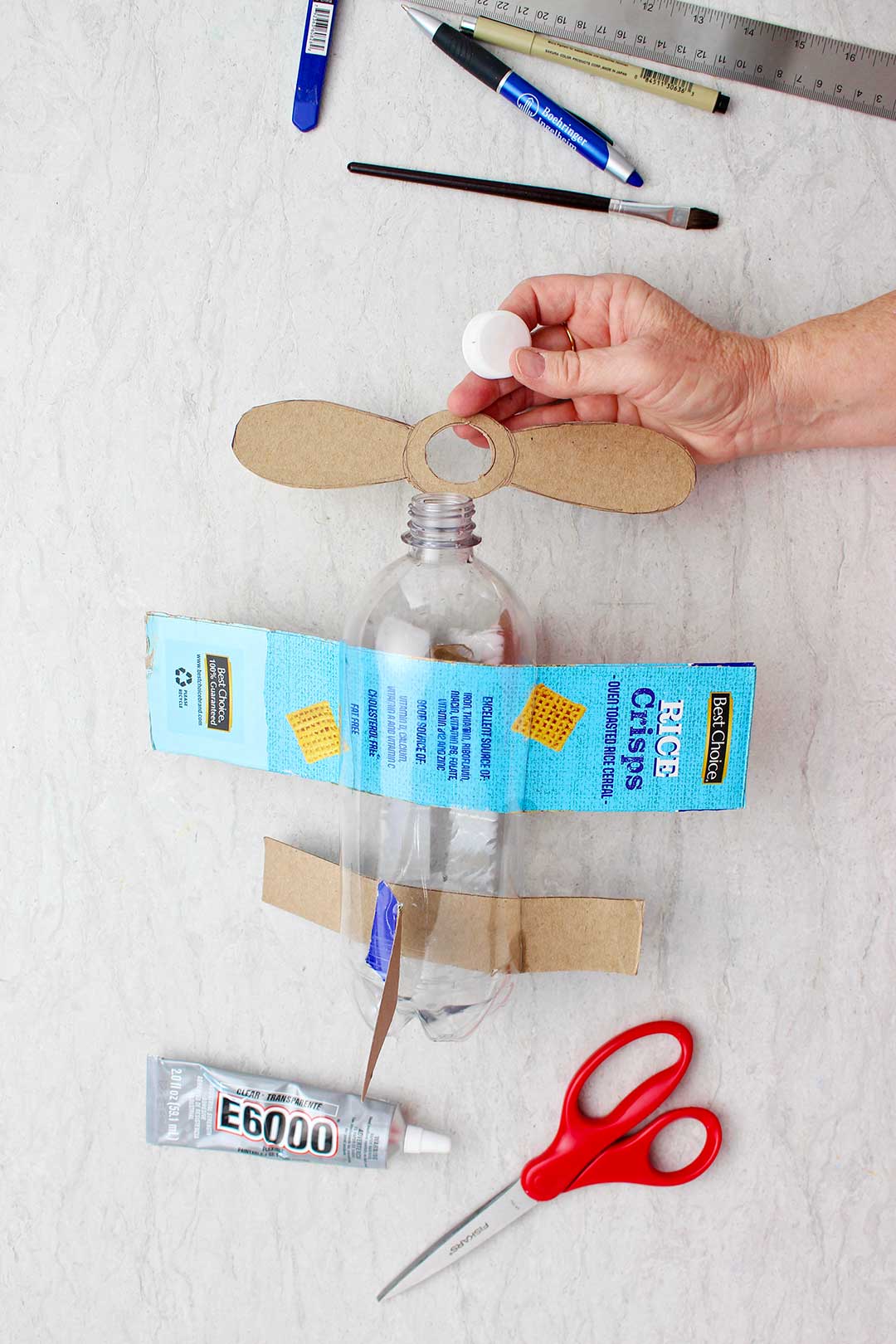 Mão fixando hélices de papelão no bocal da garrafa.