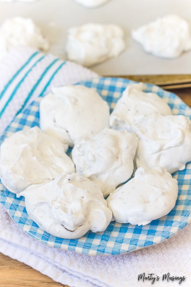 Biscoitos de merengue brancos em prato azul com biscoitos na assadeira