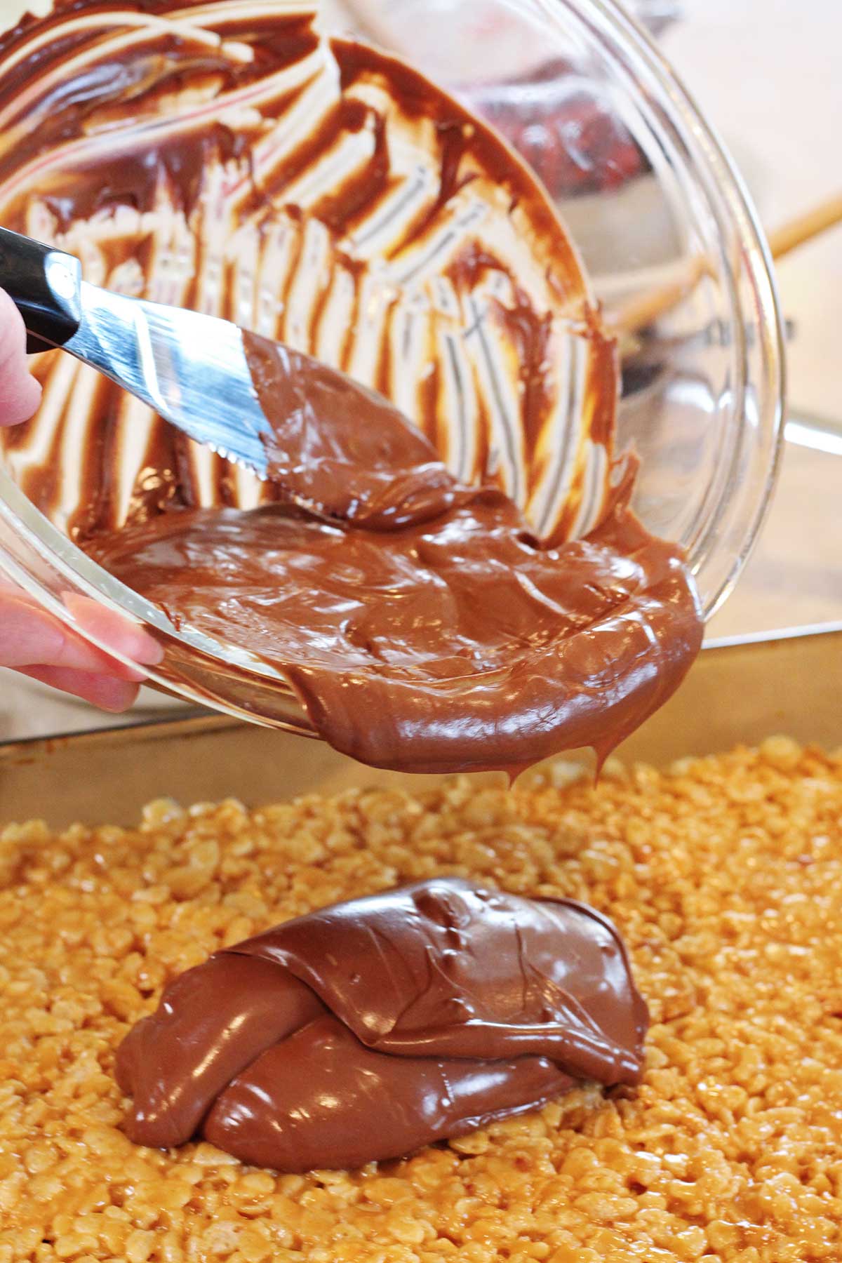 Uma pessoa despejando chocolate derretido de uma tigela sobre os scotcharoos.