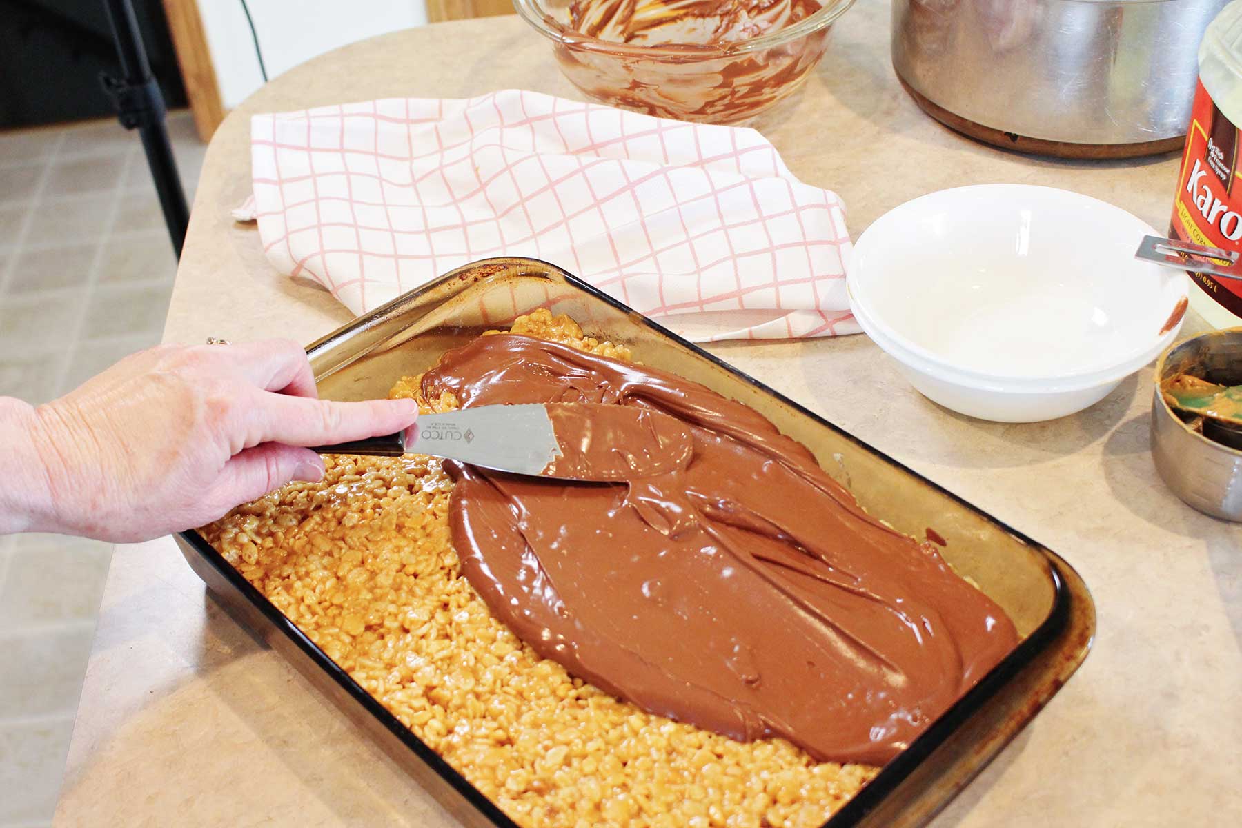 Uma pessoa usando uma espátula de metal para espalhar chocolate derretido sobre os scotcharoos.